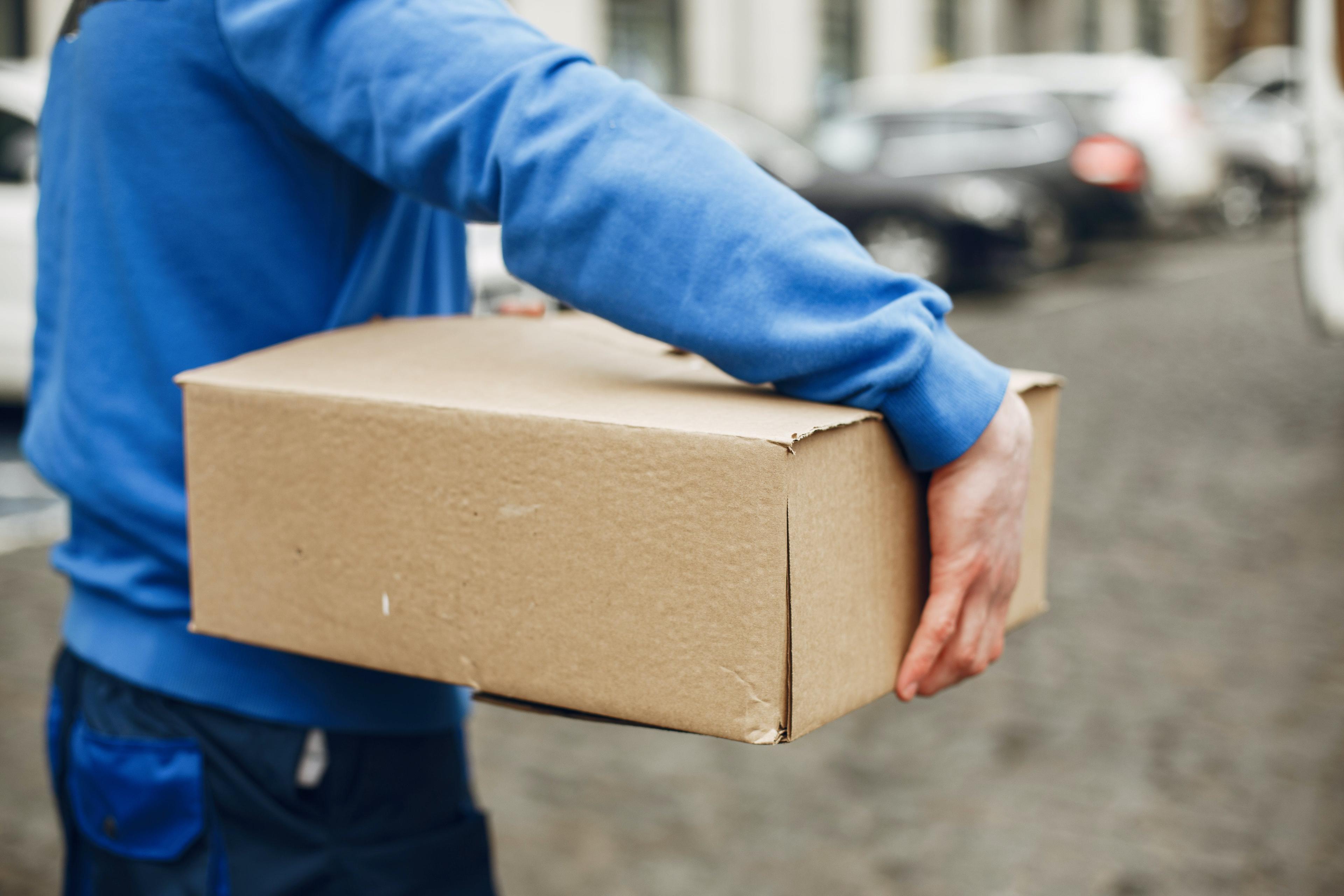 A parcel carrier wearing a blue jumper carries a parcel.