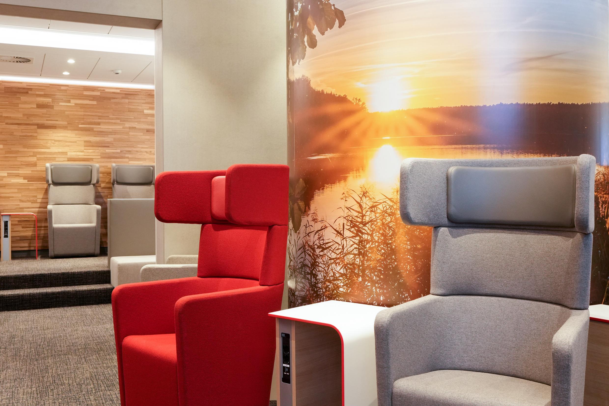 Roter und grauer Sessel vor einem Foto mit Sonnenuntergang in einer DB Lounge.