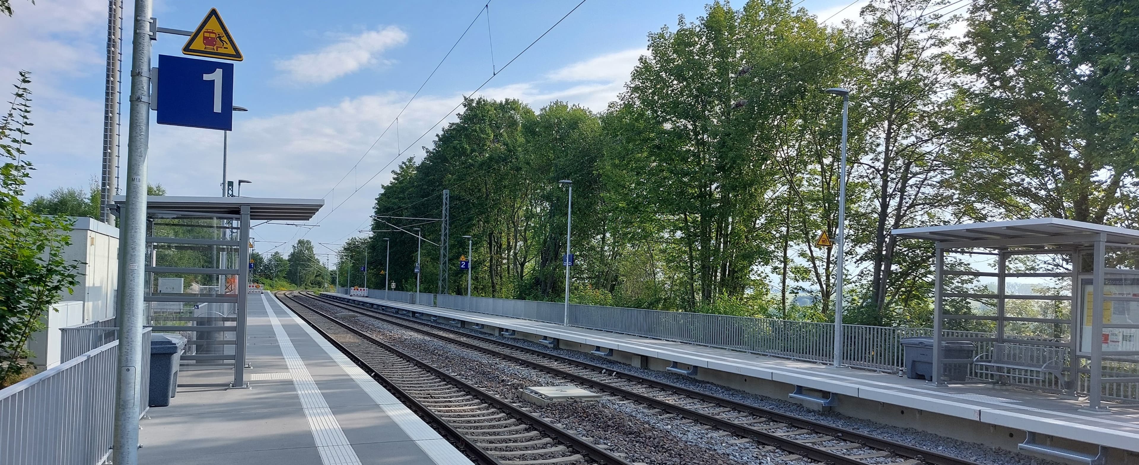 Zu sehen sind die zwei Bahnsteige mit Wetterschutzhäusern und Sitzbänken aus Metall.