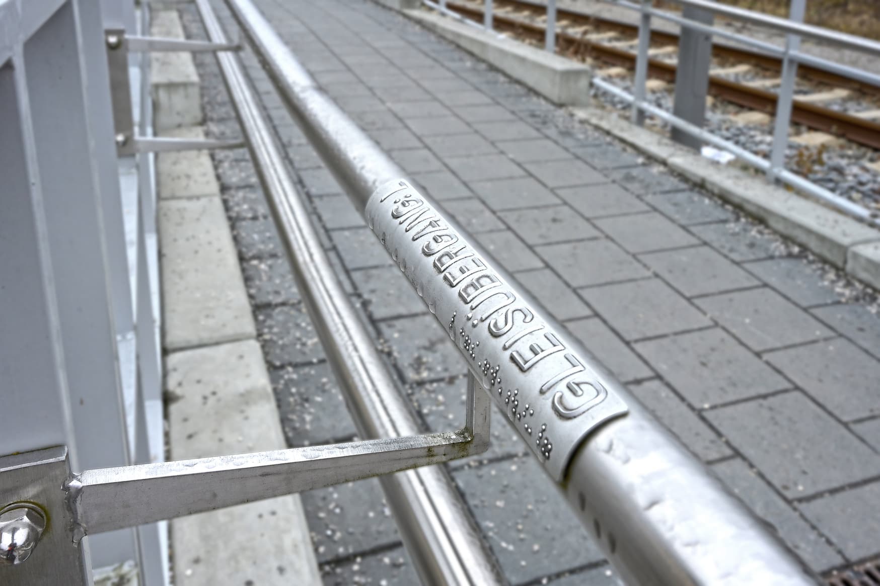 Detailaufnahme der Brailleschrift am Handlauf einer Rampe zum Bahnsteig.