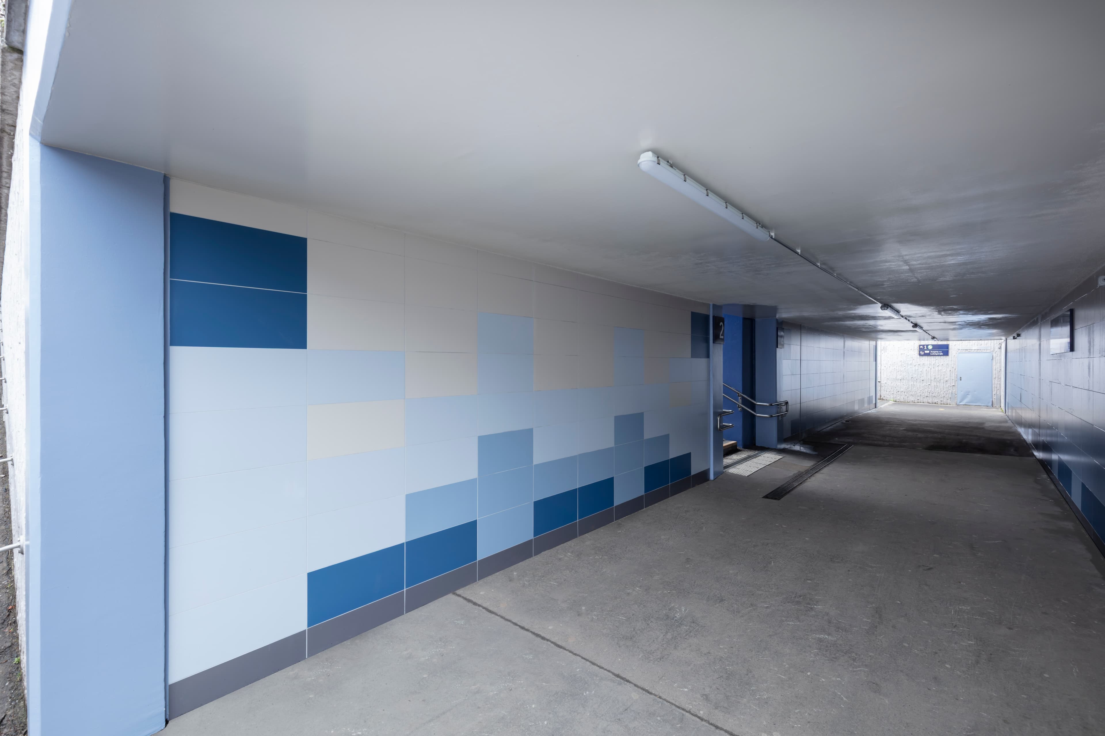 Treppe aus einer modernisierten, blau-weiß gefliesten Unterführung zum Bahnsteig, führt nach oben ins Tageslicht.