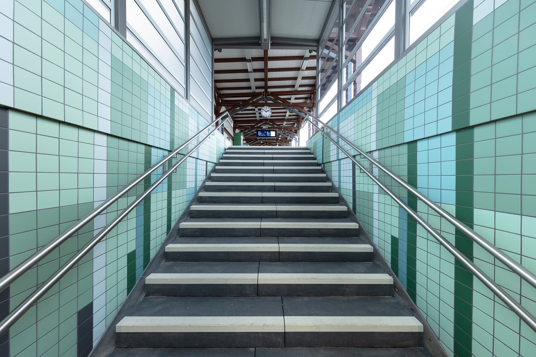 Der Treppenaufgang mit grünen Fliesen, Handlauf und Einhausung mit transparenten Scheiben.