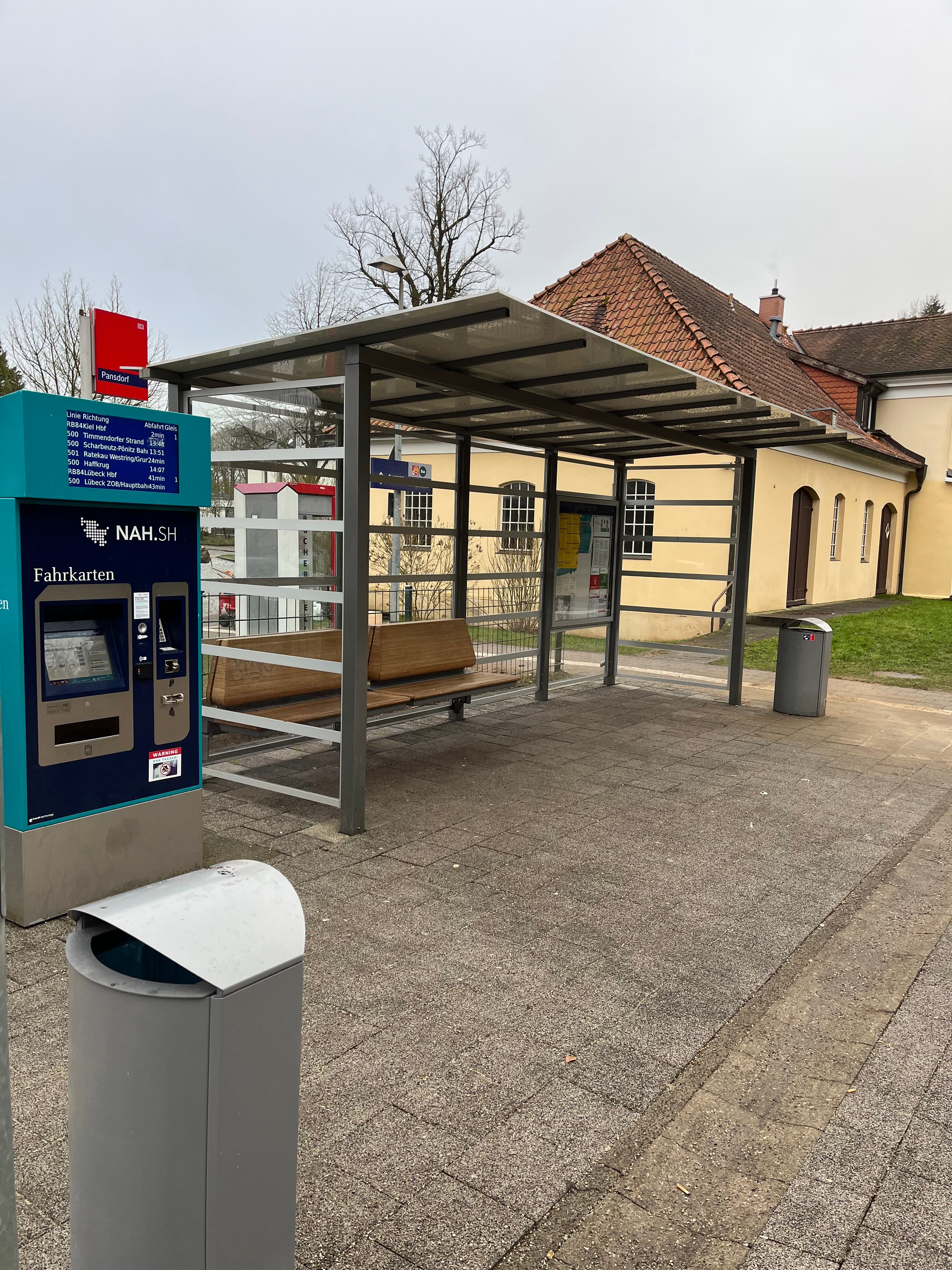 Transparenter Wetterschutz mit neuer Bank, frischen Abfallbehältern und einem Fahrkartenautomaten.