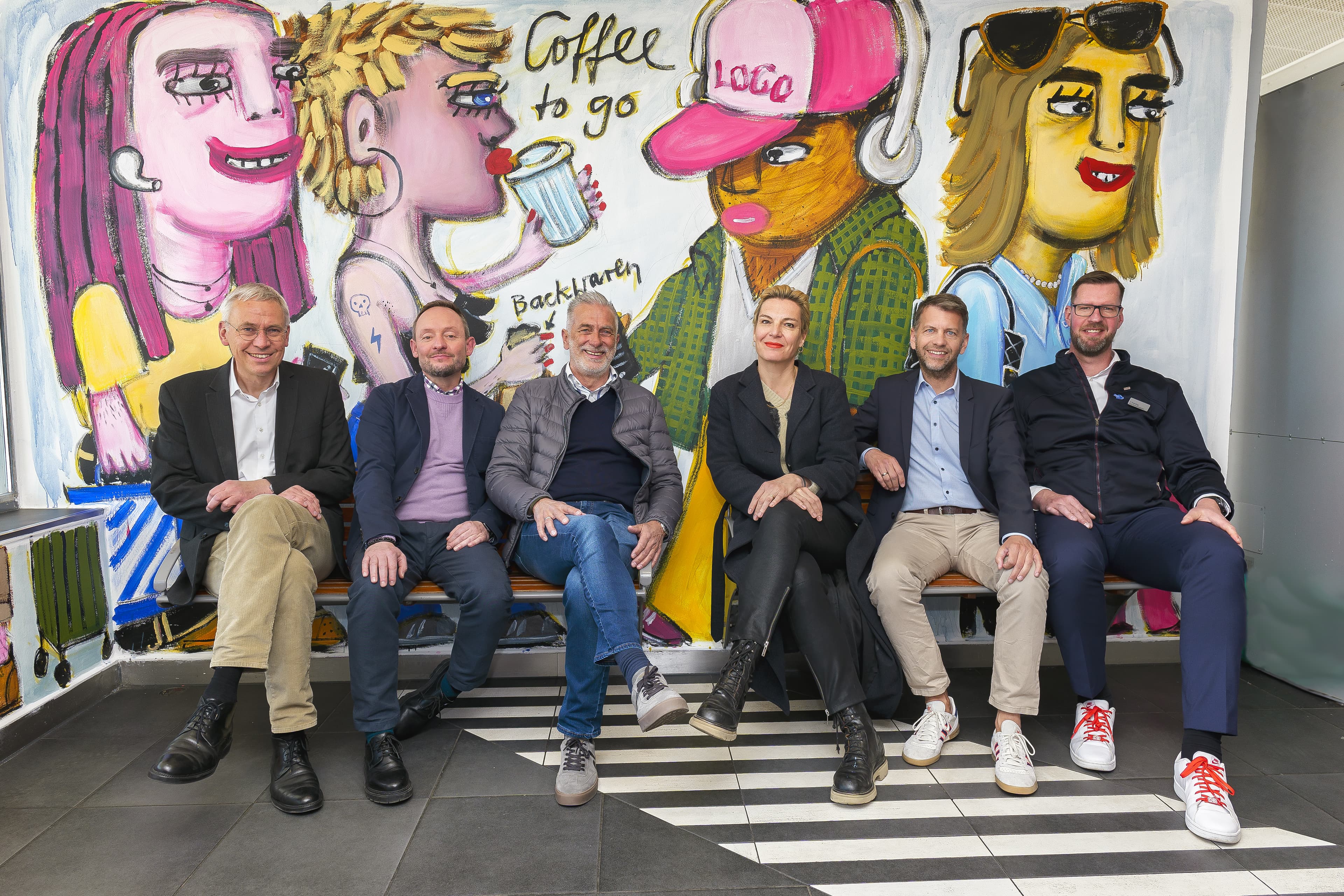 Sechs Personen sitzen vor der Installation am Bahnhof.