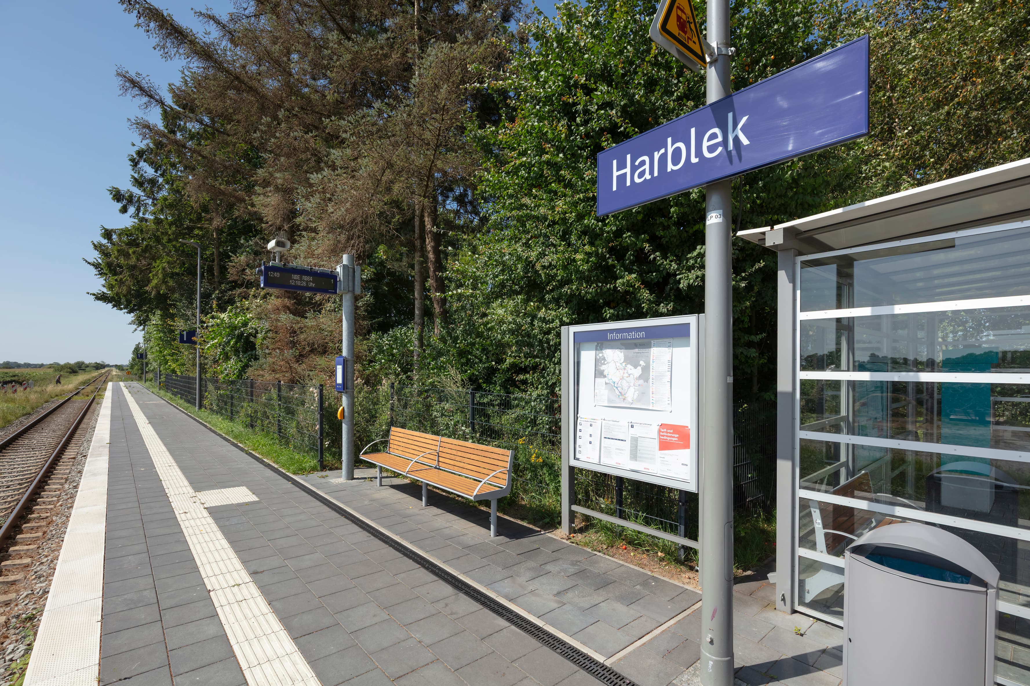 Blick auf den Bahnsteig mit Zugzielanzeiger, Sitzbank und Vitrine.