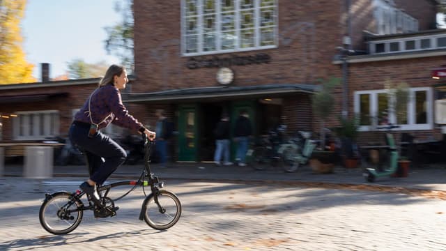 Eine junge Frau fährt mit einem Fahrrad vor den Eingang eines Bahnhofs.