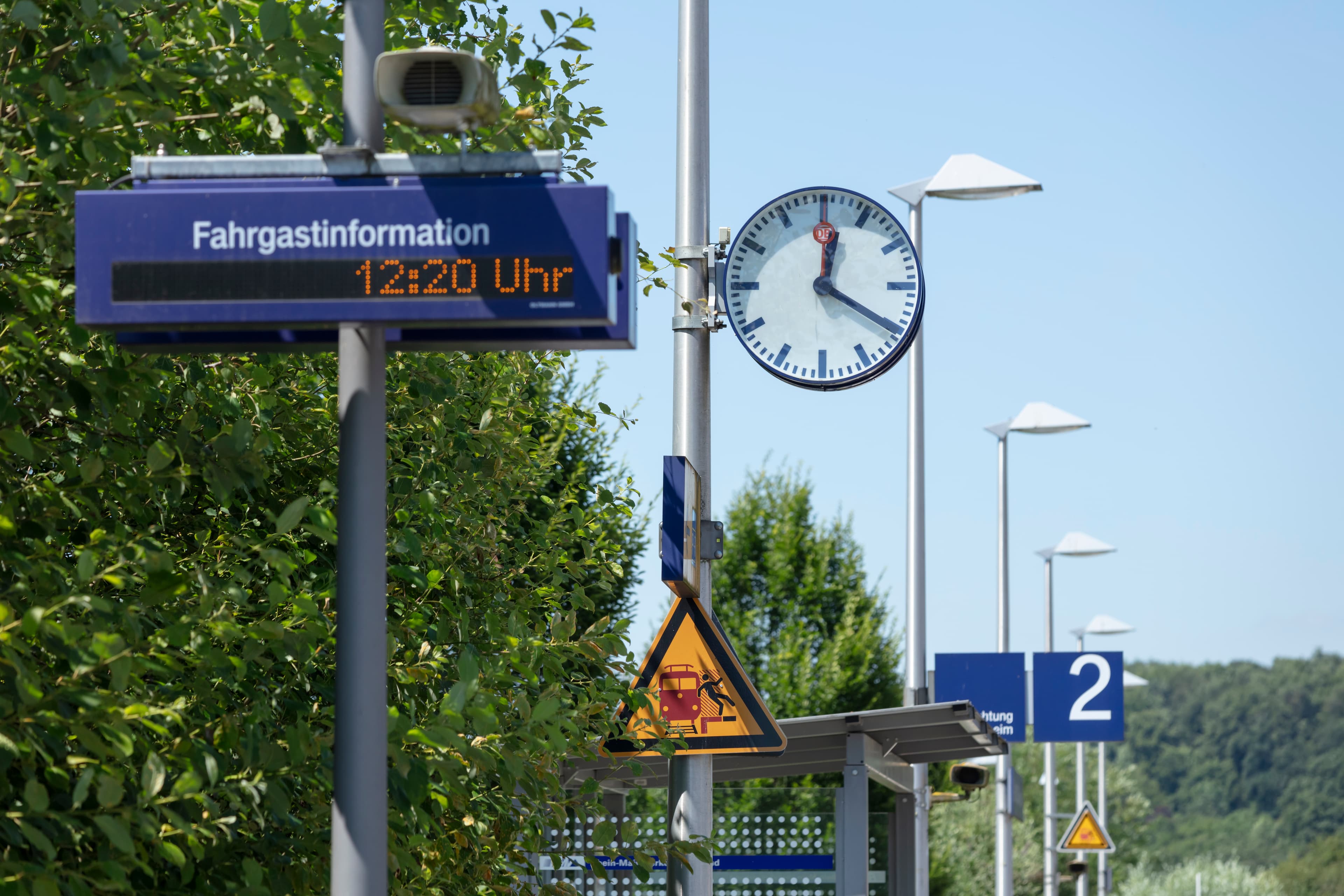 Ein einzeiliger Schriftenanzeiger, dahinter die Bahnhofsuhr und fortlaufend die Bahnsteigbeleuchtung.