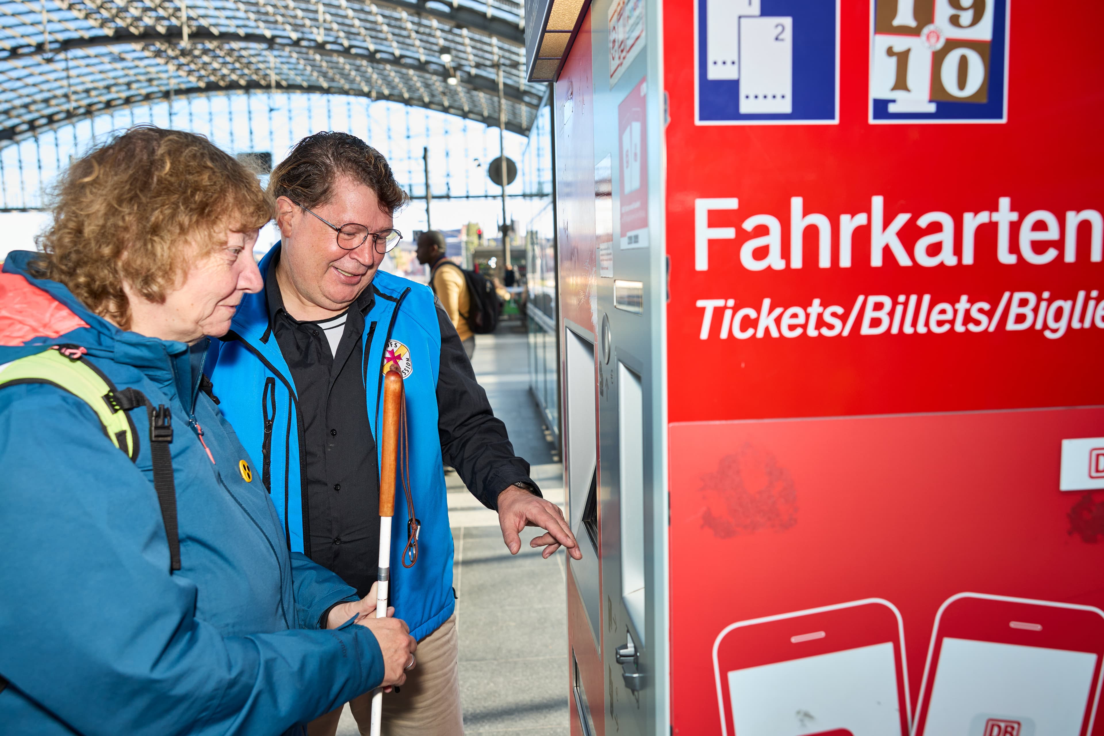 Eine Mitarbeiterin der Bahnhofsmission hilft einer Reisenden beim Ticketkauf am Automaten.