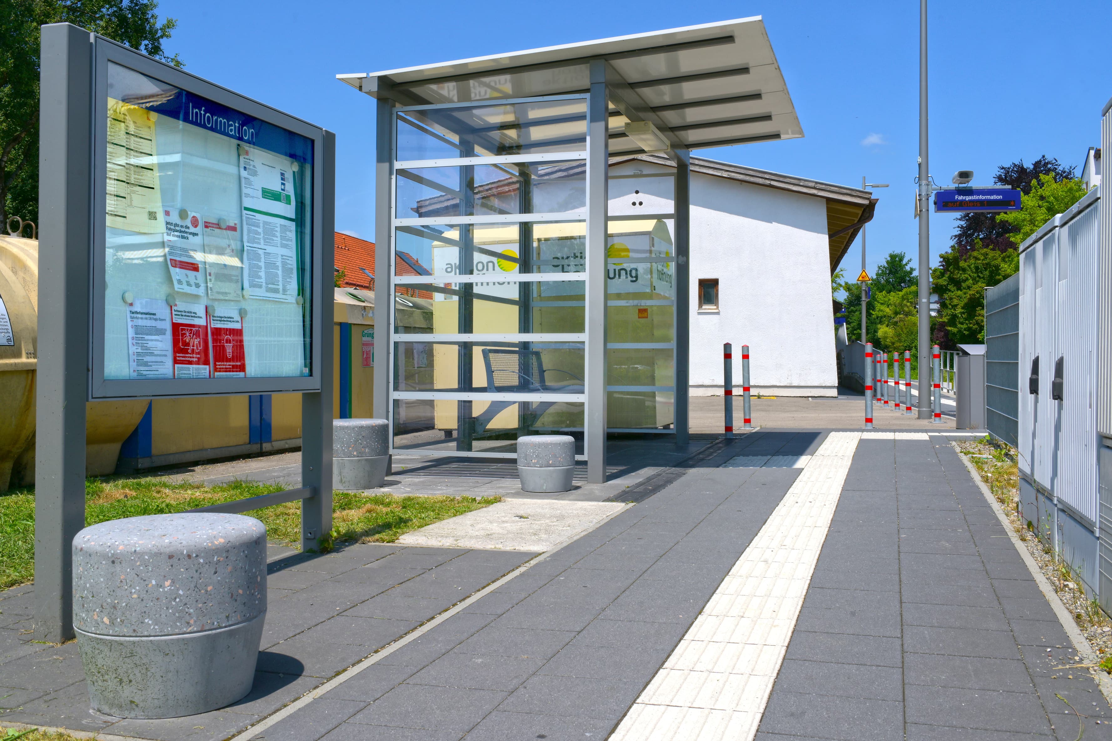 Neben einem Wetterschutzhaus und vor einer Infotafel, stehen kniehohe Betonhocker und laden zum verweilen ein.