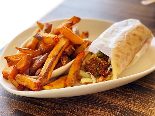 Porzellanteller mit knusprigen Pommes und einem Wrap gefüllt mit Falafel-Bällchen. 