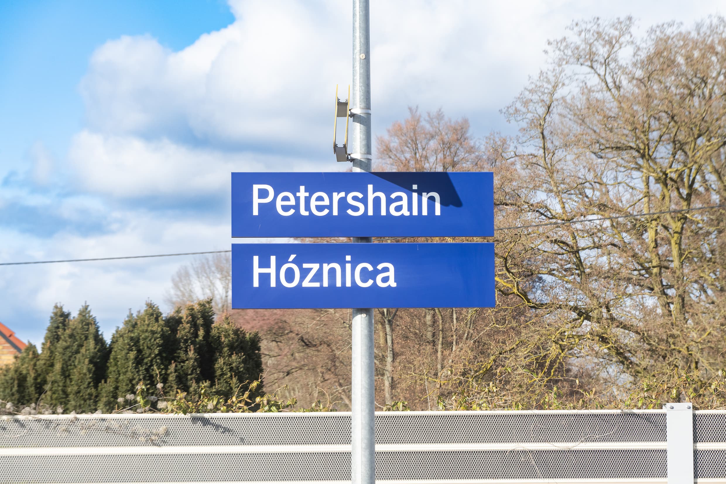 Bahnhofsnamensschilder in deutsch (Petershain) und sorbisch (Hóznica). weiße Schrift auf dunkelblauem Untergrund.