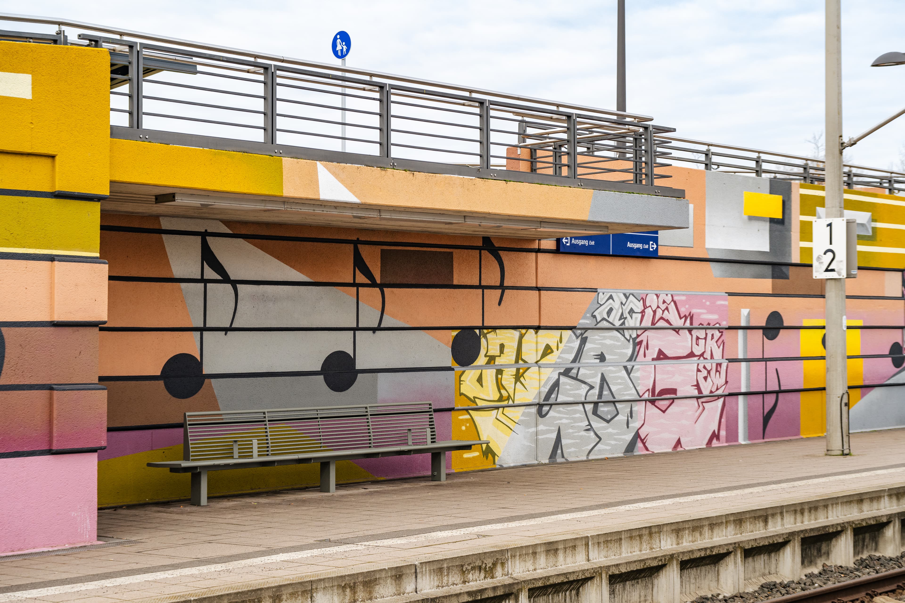 Bunte Gestaltung der Wände vorwiegend mit den Farben gelb, orange und pink inkl. Graffitischriftzügen und Musiknoten. In einer steht eine graue Stahlrohrbank.