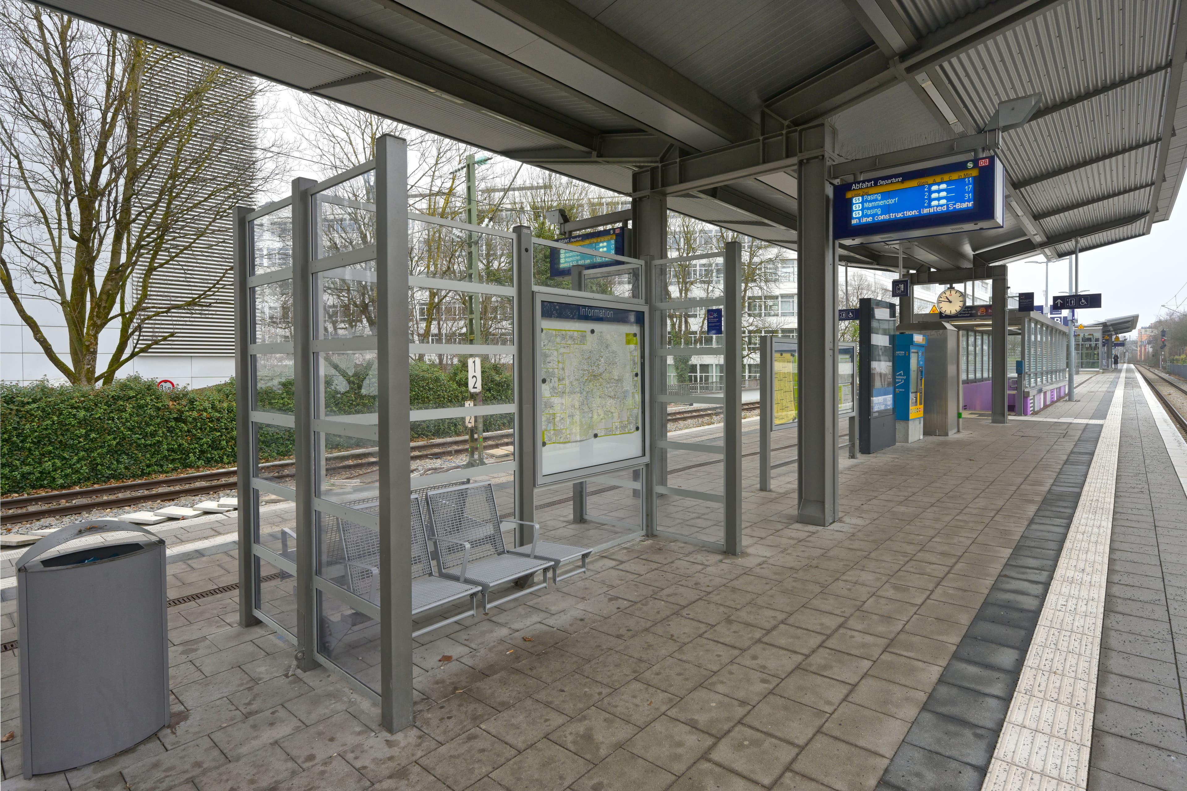 Blick auf den Bahnsteig mit einem volltransparenten Wetterschutzanlage und gestalteter Treppeneinhausung im Hintergrund