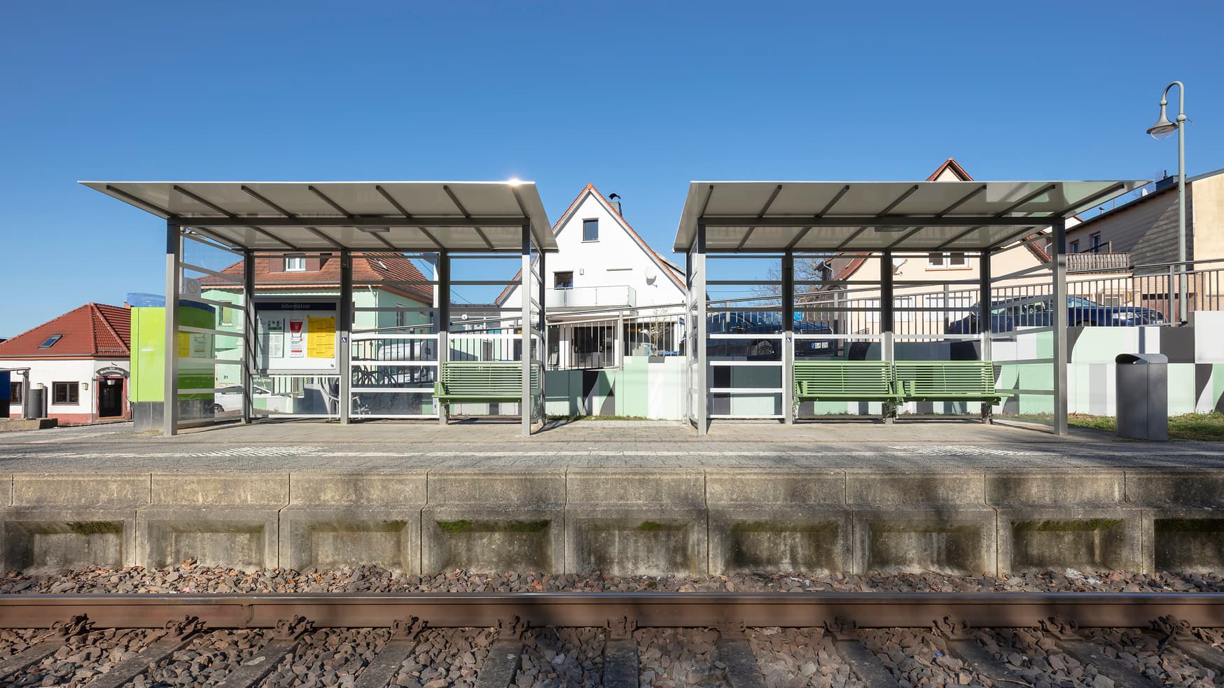 Blick auf zwei Wetterschutzhäuschen mit Sitzgelegenheiten. Davor befindet sich der Bahnsteig und das Gleis.