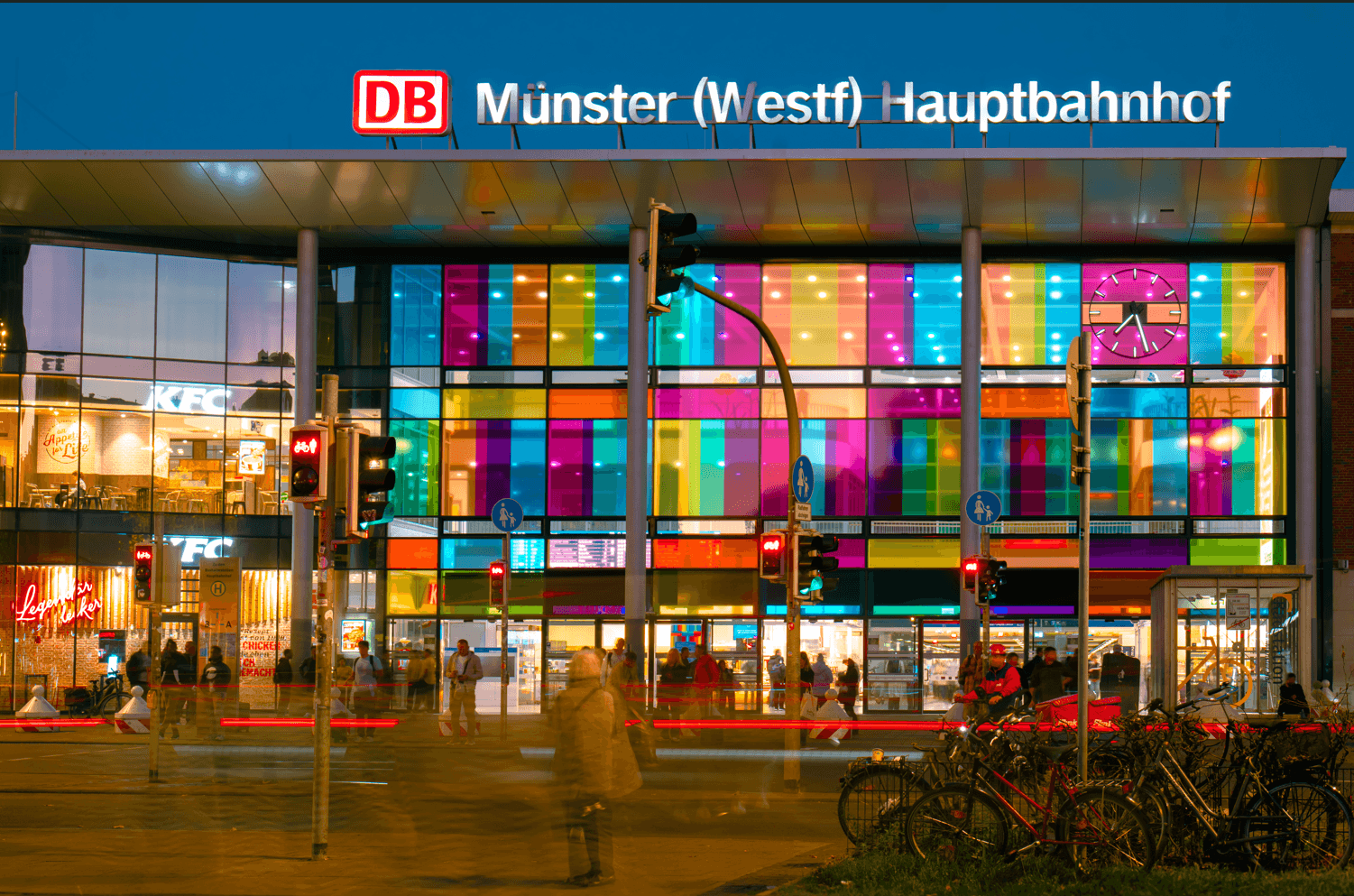 Bahnhof von außen mit bunten Fenstern in der Dämmerung.