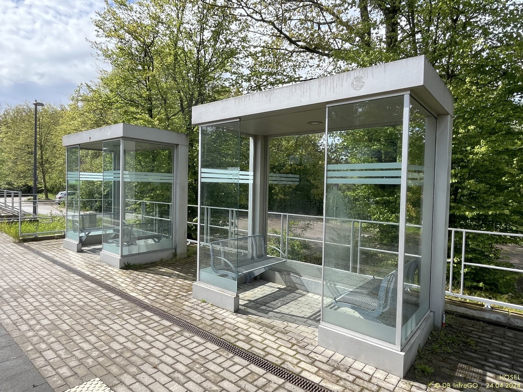 Zwei Wetterschutzhäuser mit Betonfassung und Glaspanelen.