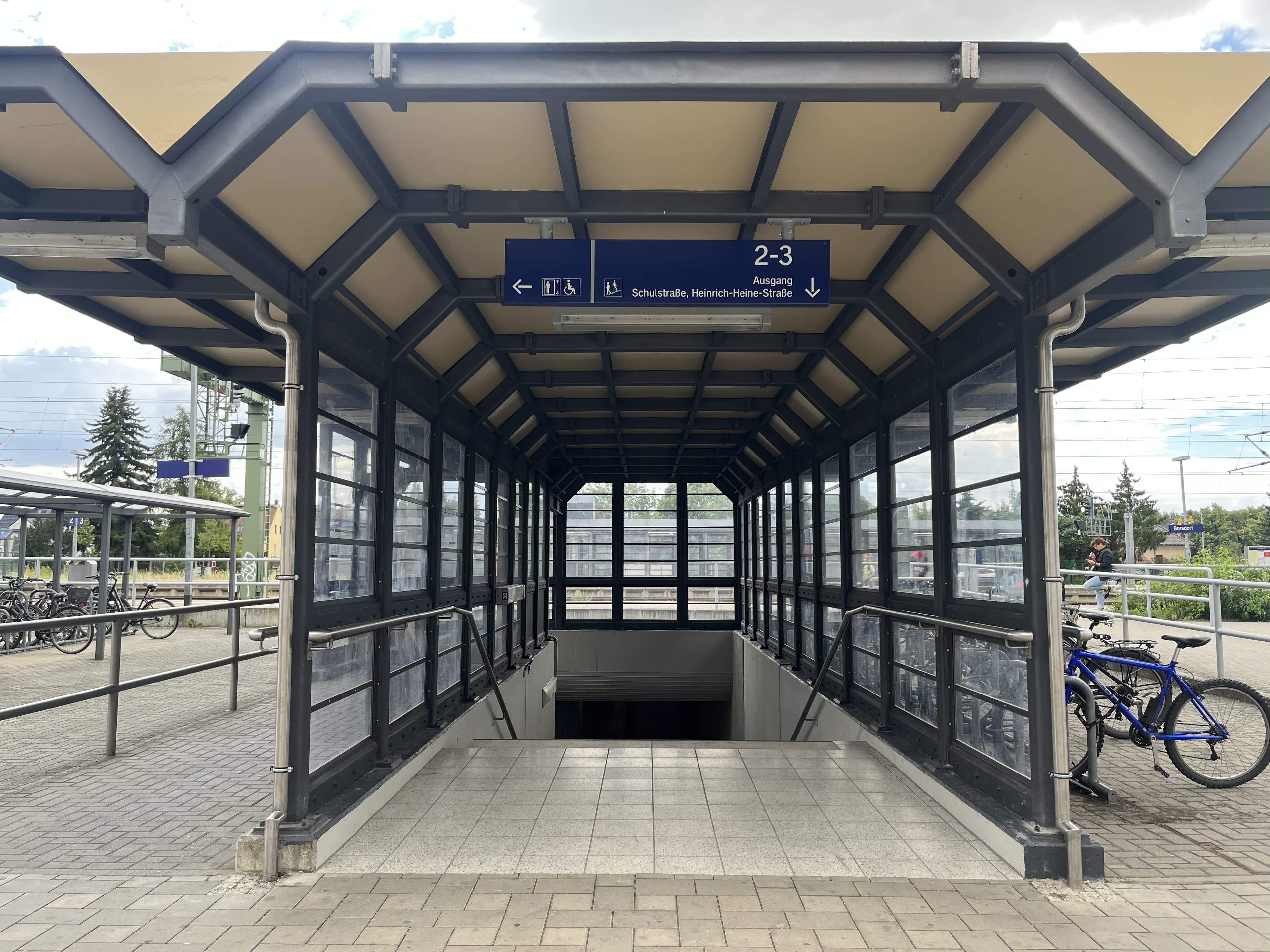 Zu sehen ist ein vollständig verglaster Treppenzugang mit dunklem angestrichen Metallrahmen. Der Boden neu gefliest. 