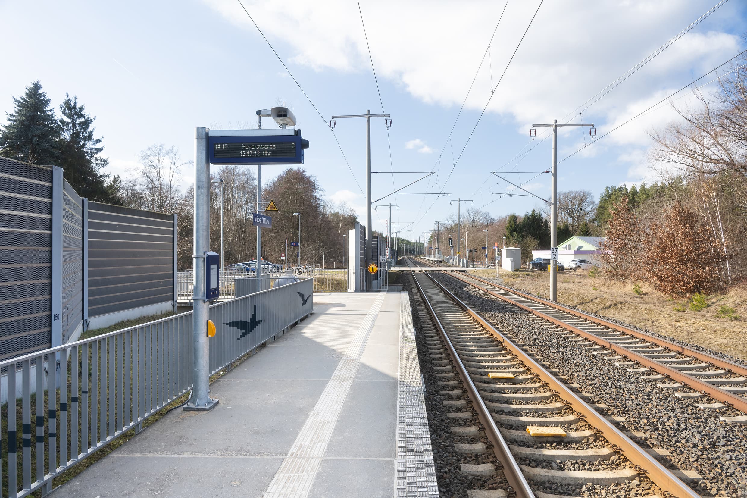 Blick auf den Bahnsteig mit dem neuen zweizeiligen Anzeiger, einem digitalen Bauaushang mit den gestalteten Geländern im Hintergrund.