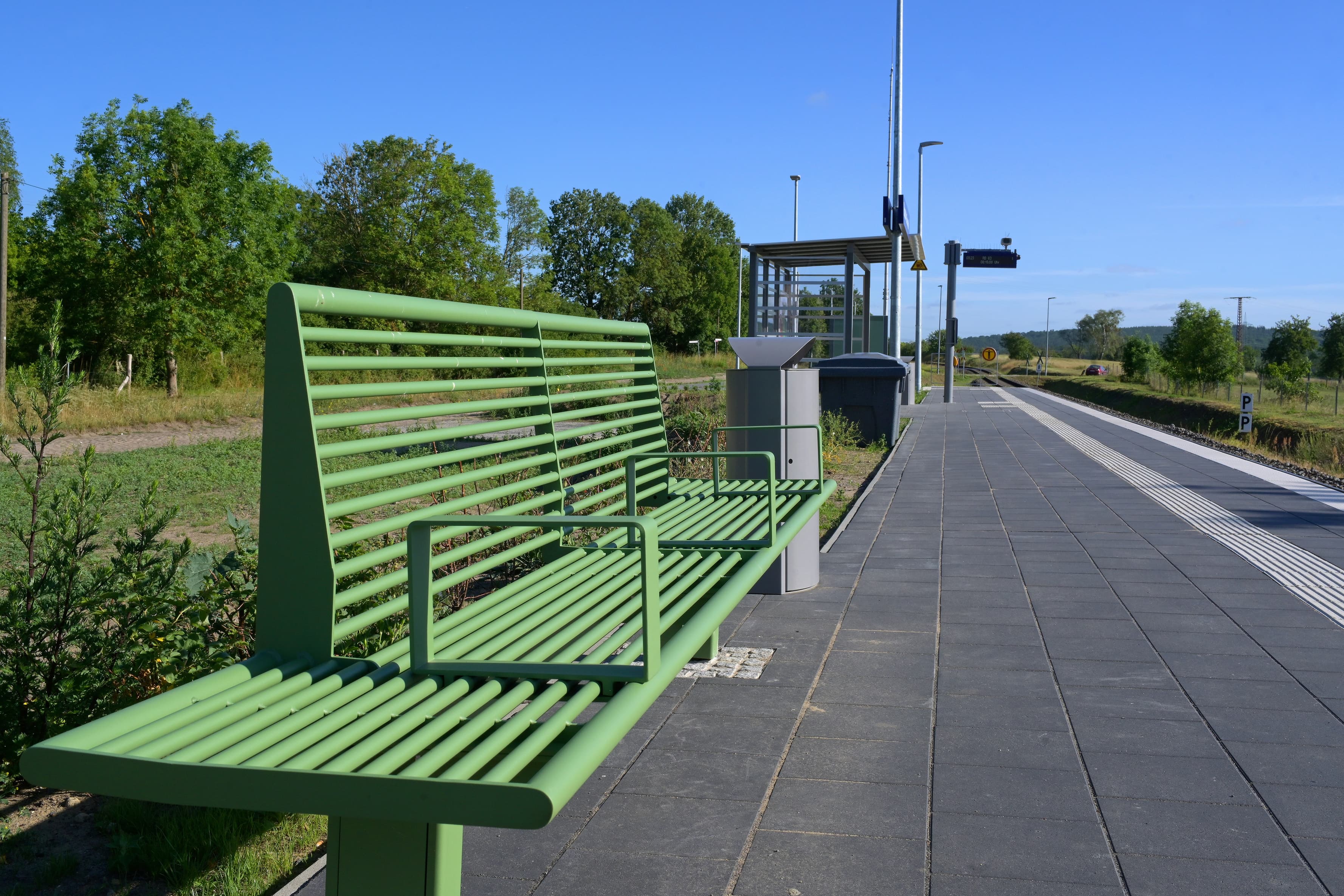 Eine grüne Bank auf einem Bahnsteig.