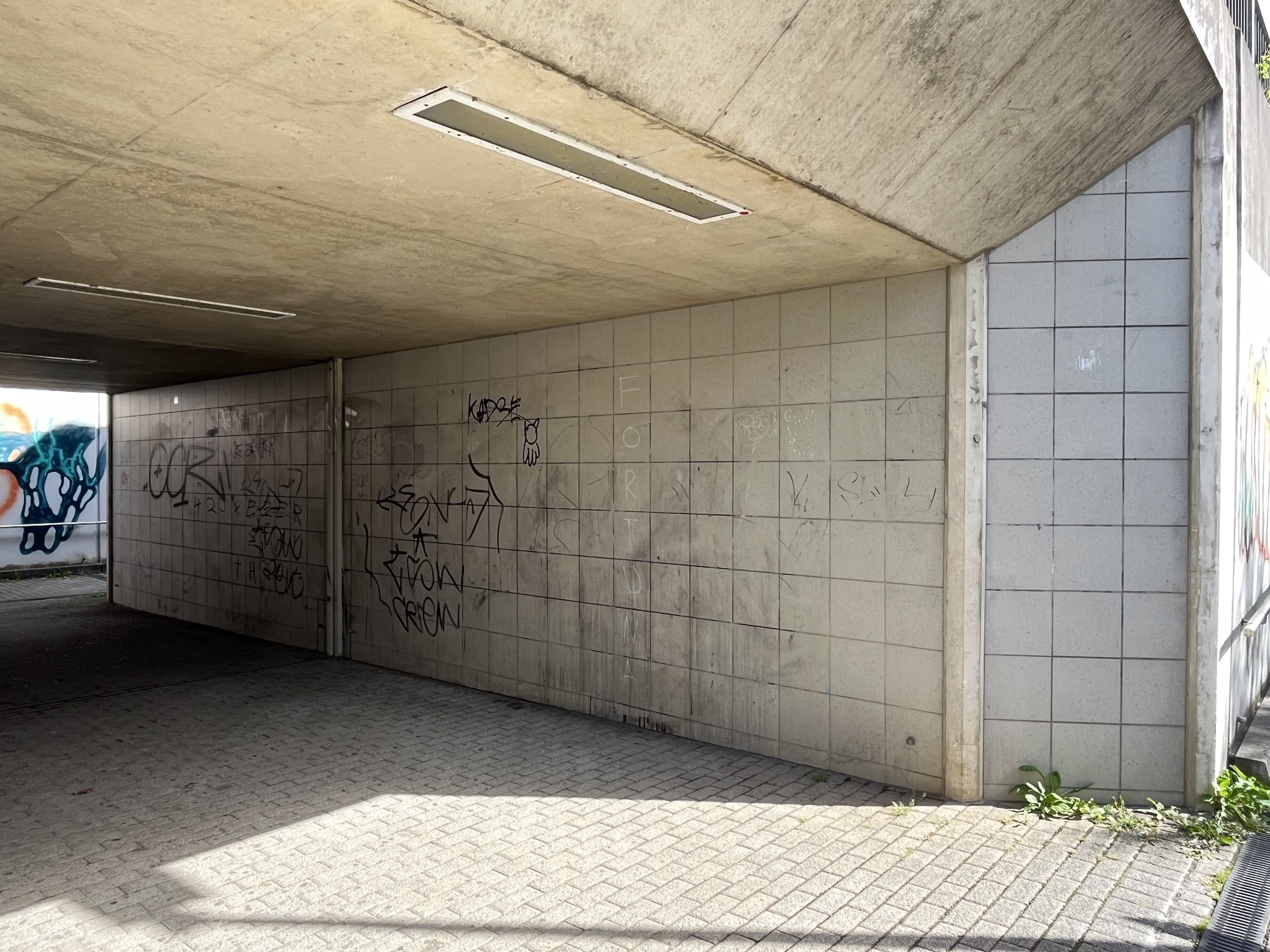 Blick auf eine grau geflieste Wand in der Personenunterführung mit Vandalismusschäden.