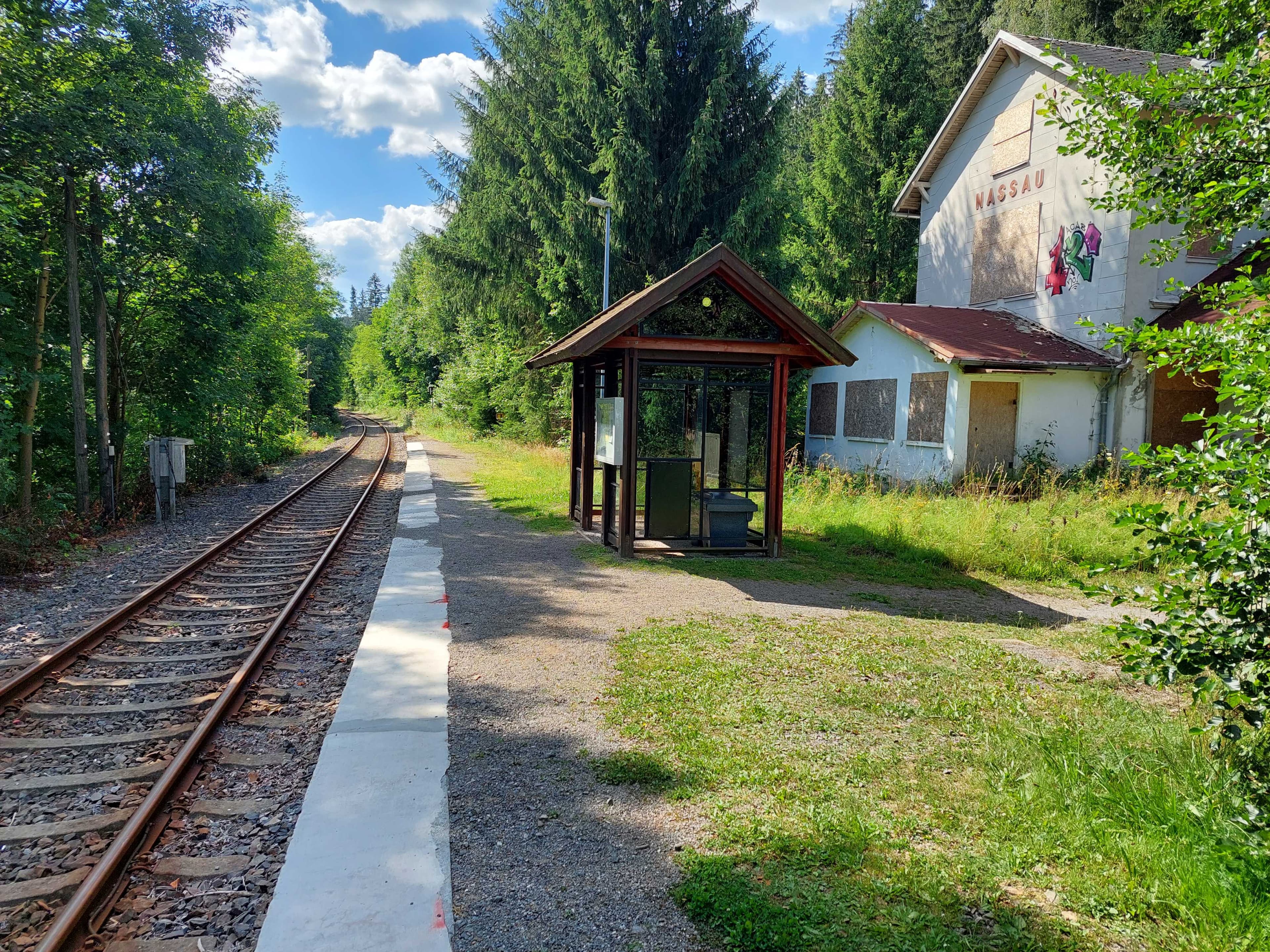 Ein Bild vor dem Umbau der Station mit einem alten Wetterschutzhaus und einem weißem Gebäude im Hintergrund.