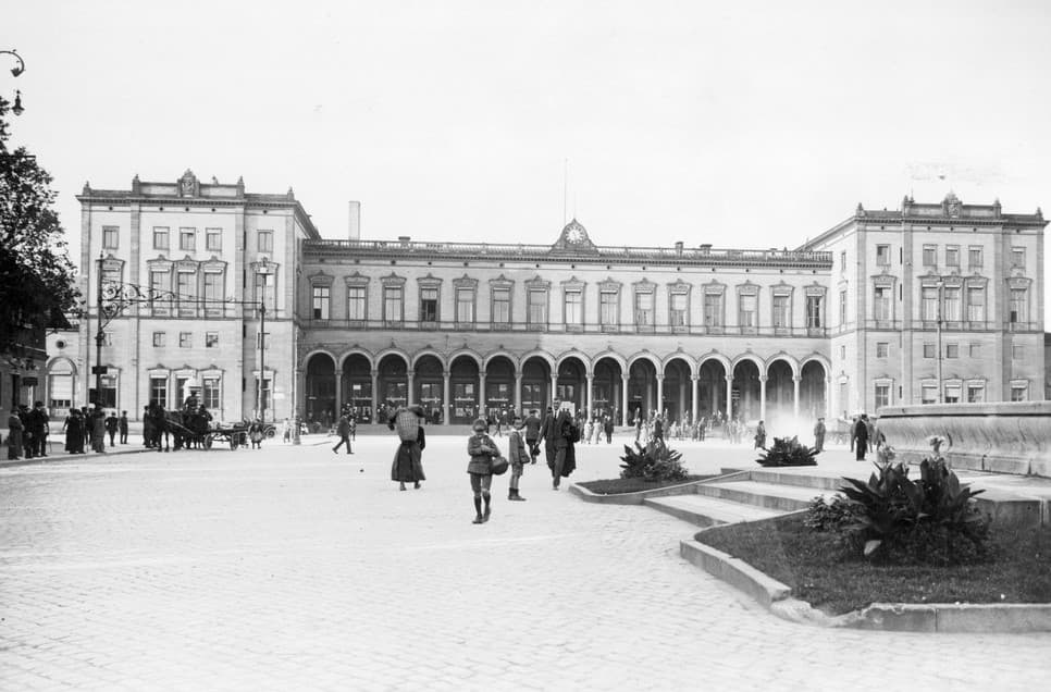 Eine Frontalansicht des Würzburger Hauptbahnhofs um 1930, ein großer Platz mit einigen Menschen und ein großes Empfangsgebäude im Hintergrund.