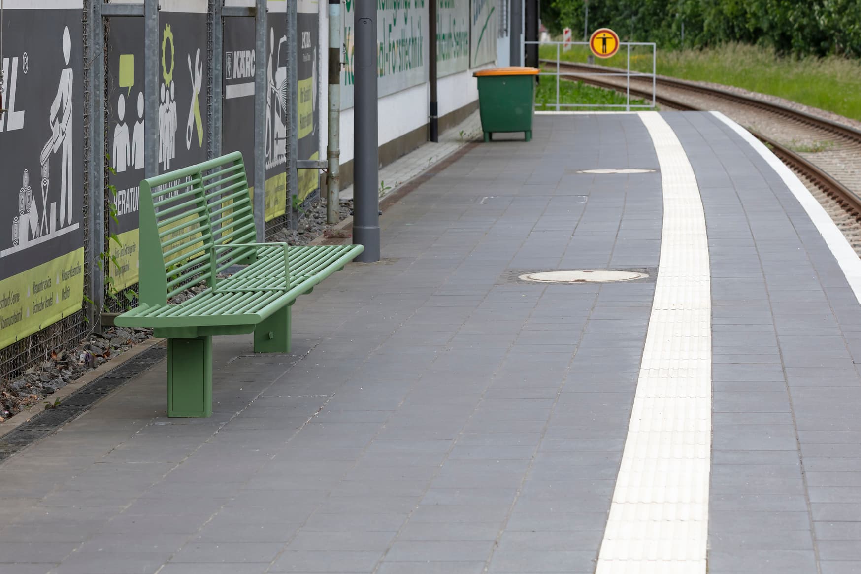 Grüne Sitzbank am Bahnsteig.