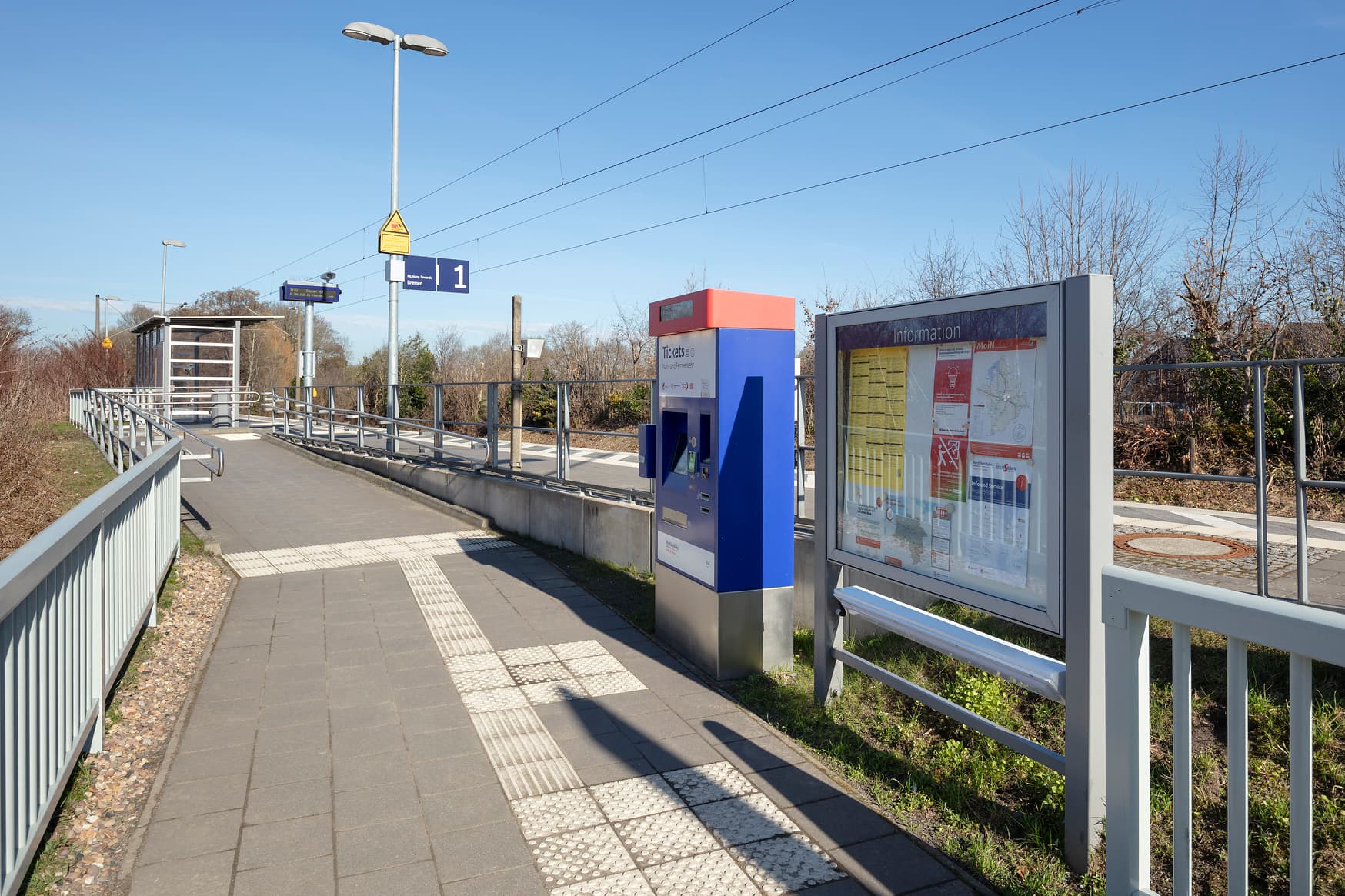 Im Bild der neu gepflasterte Weg zum Bahnsteig in Hoyenkamp. Rechts ein blauer Ticketautomat.