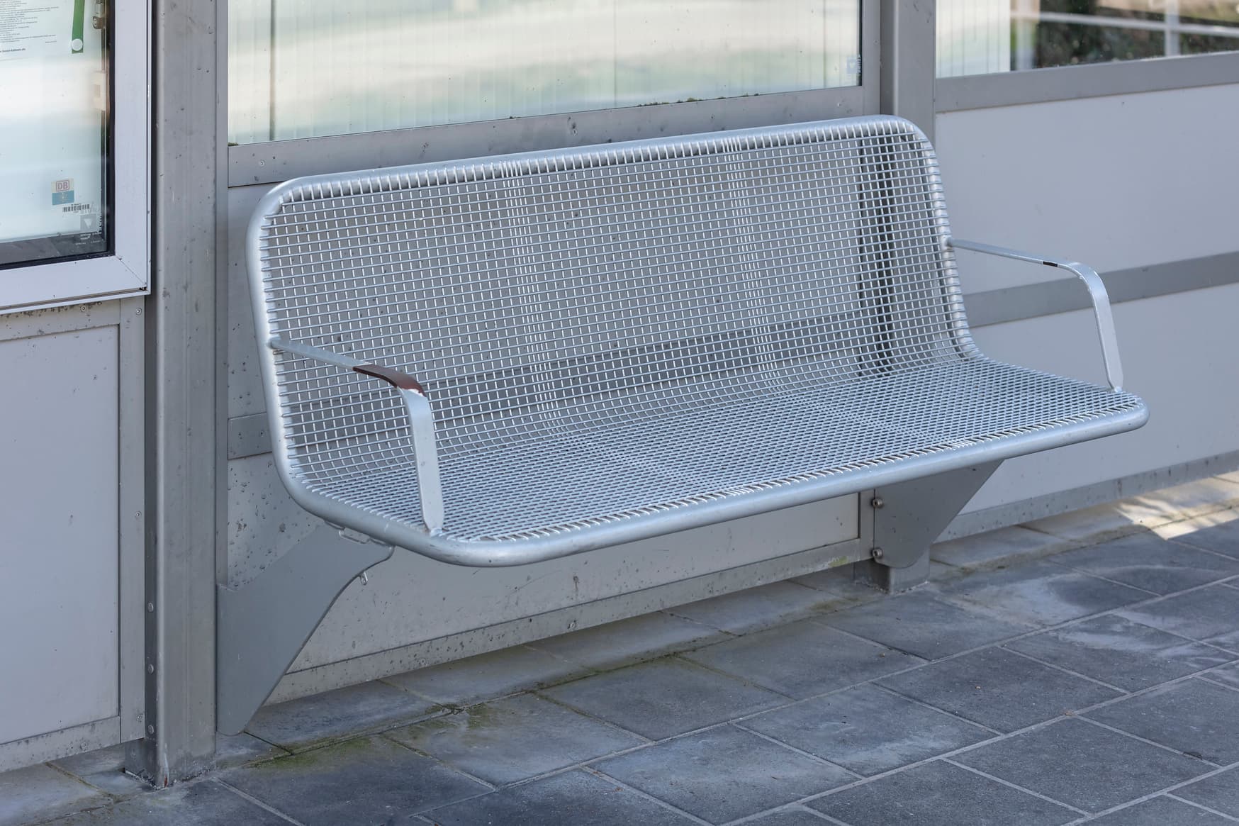 Eine graue Metall-Sitzbank im Wetterschutzhäuschen.