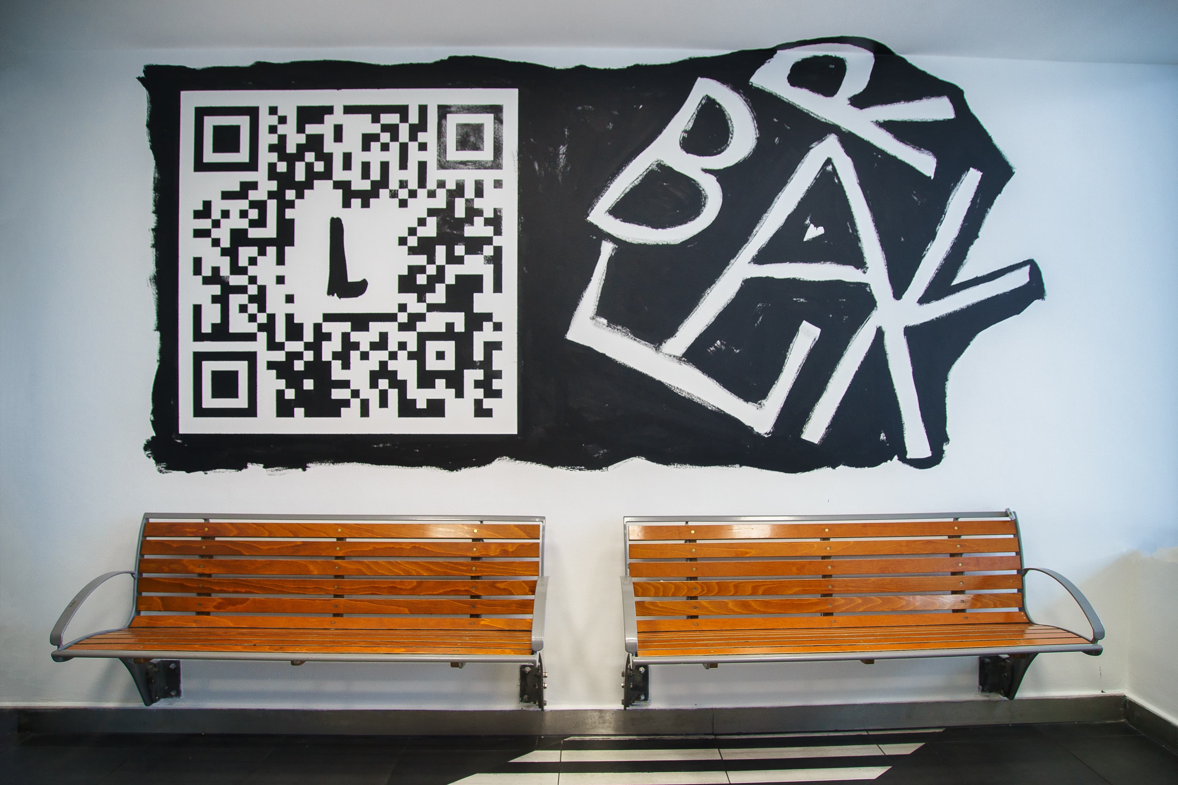 A large QR code on the wall in front of two wooden benches.