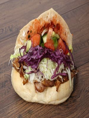 Fladenbrot gefüllt mit Dönerfleisch, Kraut, Tomate, Gurke und würziger Sauce liegt auf einem Tisch in Holzoptik.