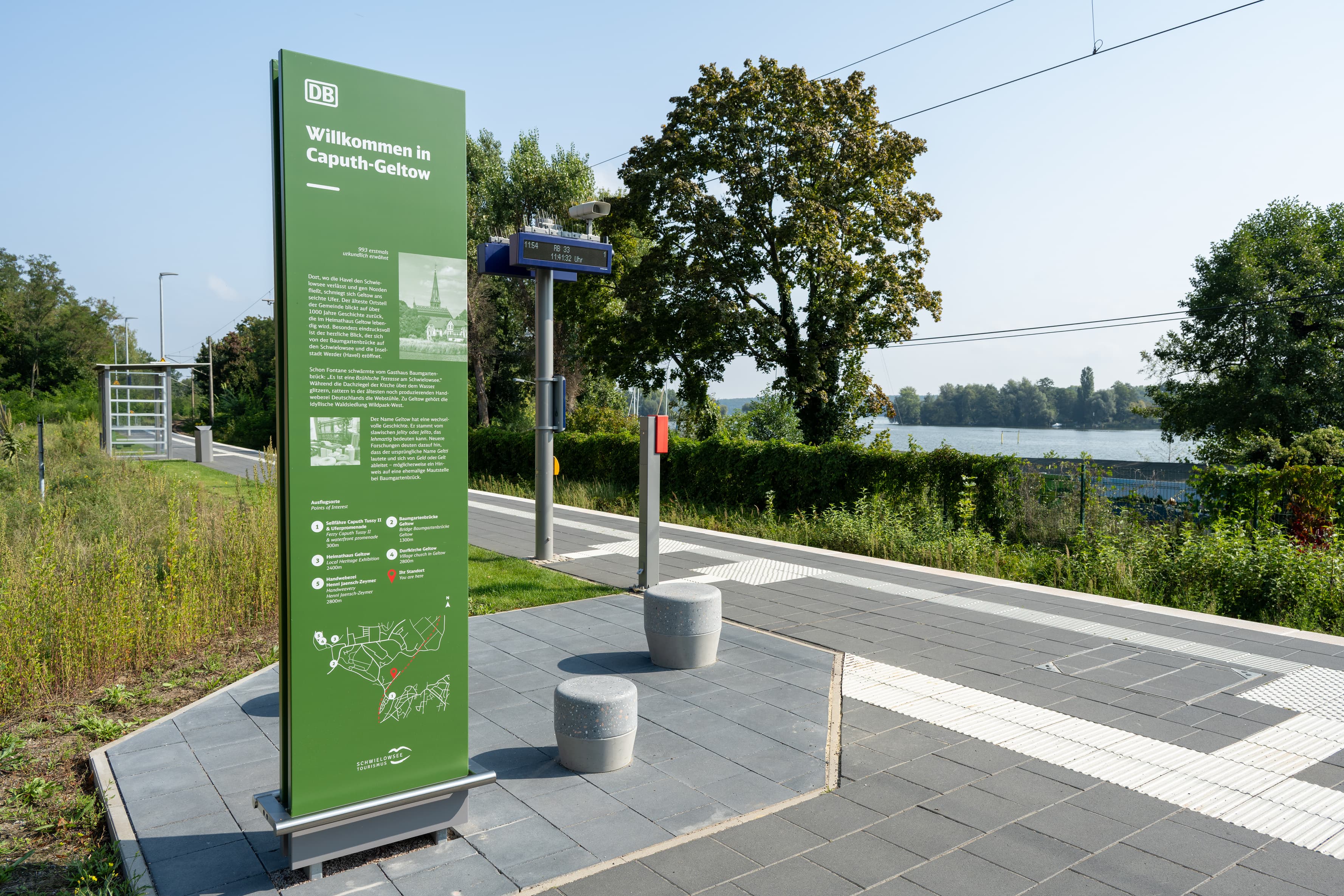 Betonhocker und eine grüne Infostele an einem Bahnsteig.