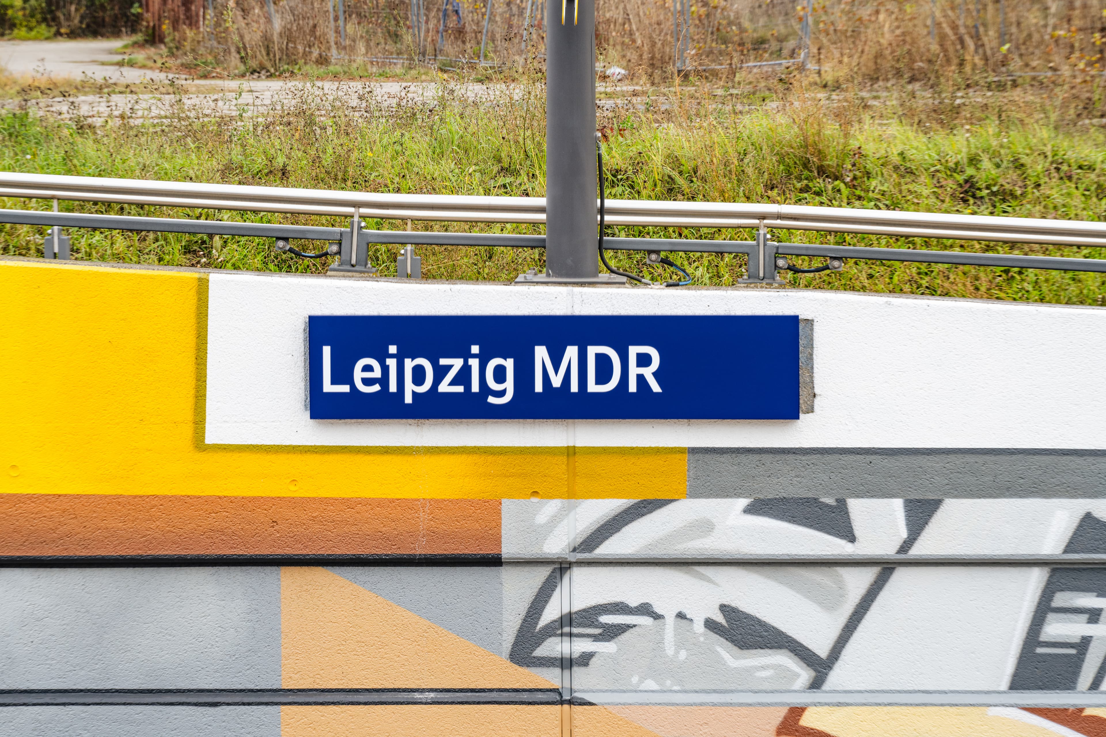 Bahnhofsnamensschild auf gestalteter Wand.