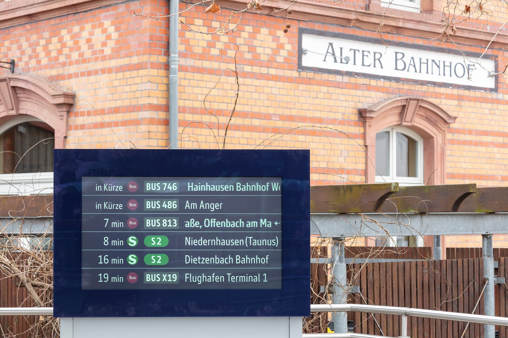 Blick auf den ZugInformationsMonitor (ZIM). Dahinter befindet sich ein Gebäude mit der Aufschrift "Alter Bahnhof". 