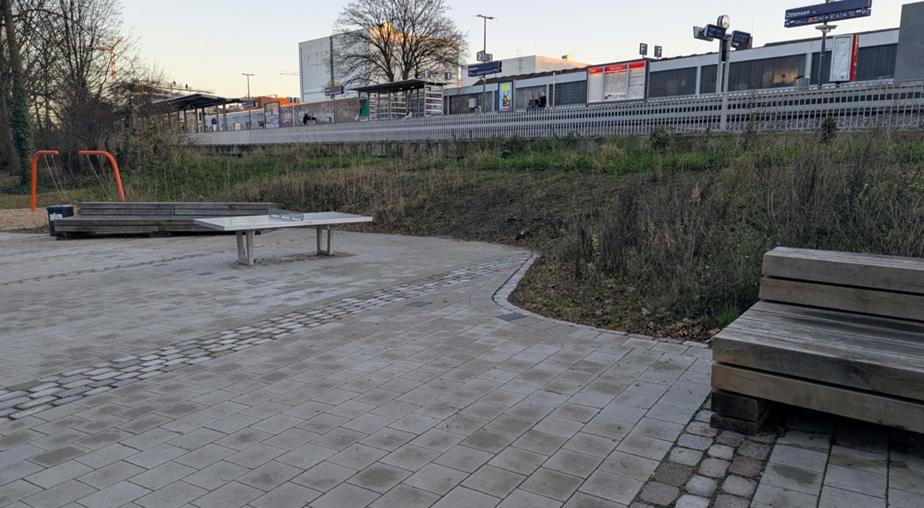 Pflasterung, Tischtennisplatte und Holzbank.