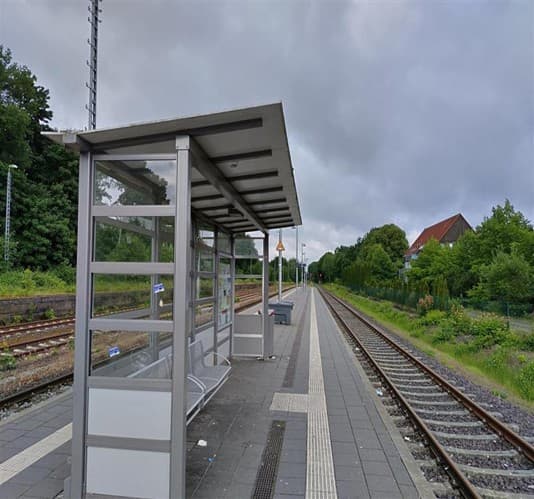 Wetterschutzhäuschen auf einem Bahnsteig. Daneben jeweils Gleise.