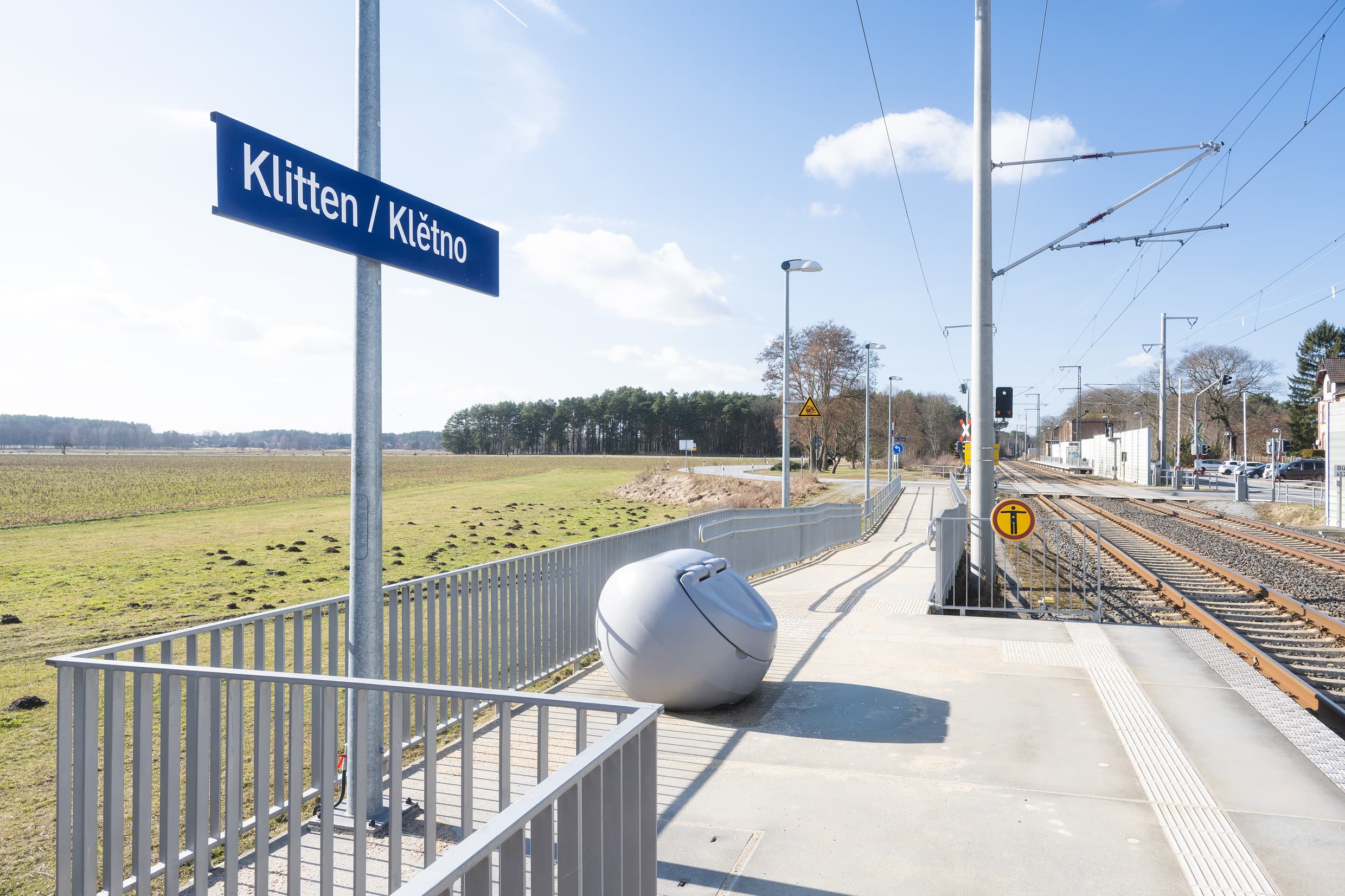 Blick auf den Zugangsbereich zu einem Bahnsteig inkl. aufgestellter Streugutbox und dem zweisprachigem Stationsnamensschild auf deutsch und sorbisch (Klitten/Kletno).