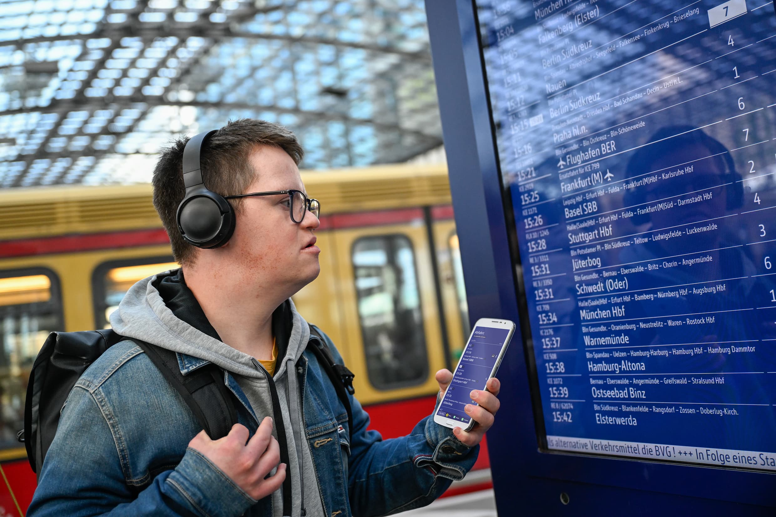 Junger Mann mit kognitiver Beeinträchtigung nutzt u.a. sein Smartphone, um sich am Bahnhof selbstständig zu orientieren und zu informieren. 