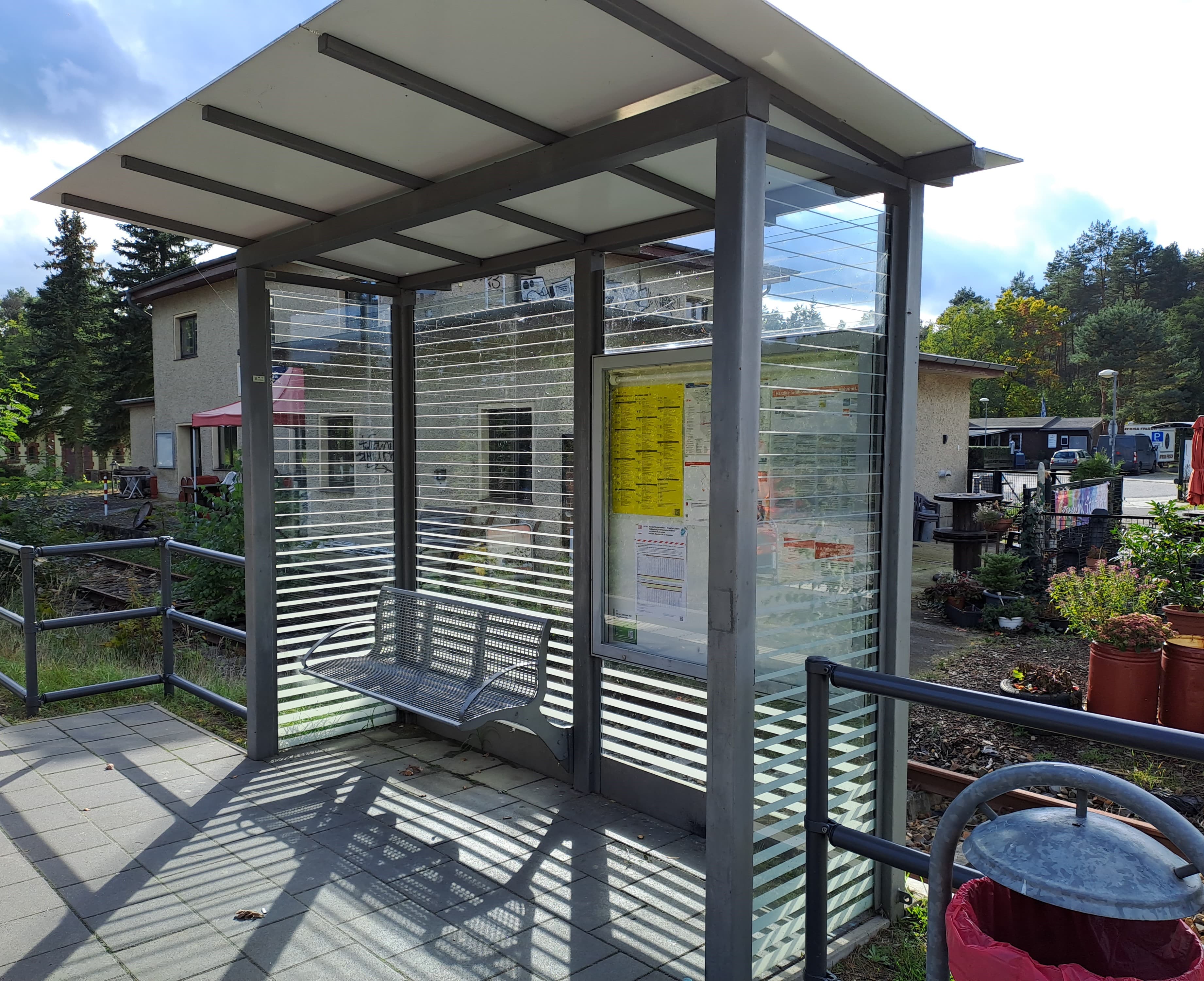 Blick auf ein Wartehaus mit grauer Sitzbank, rechts ein Mülleimer.
