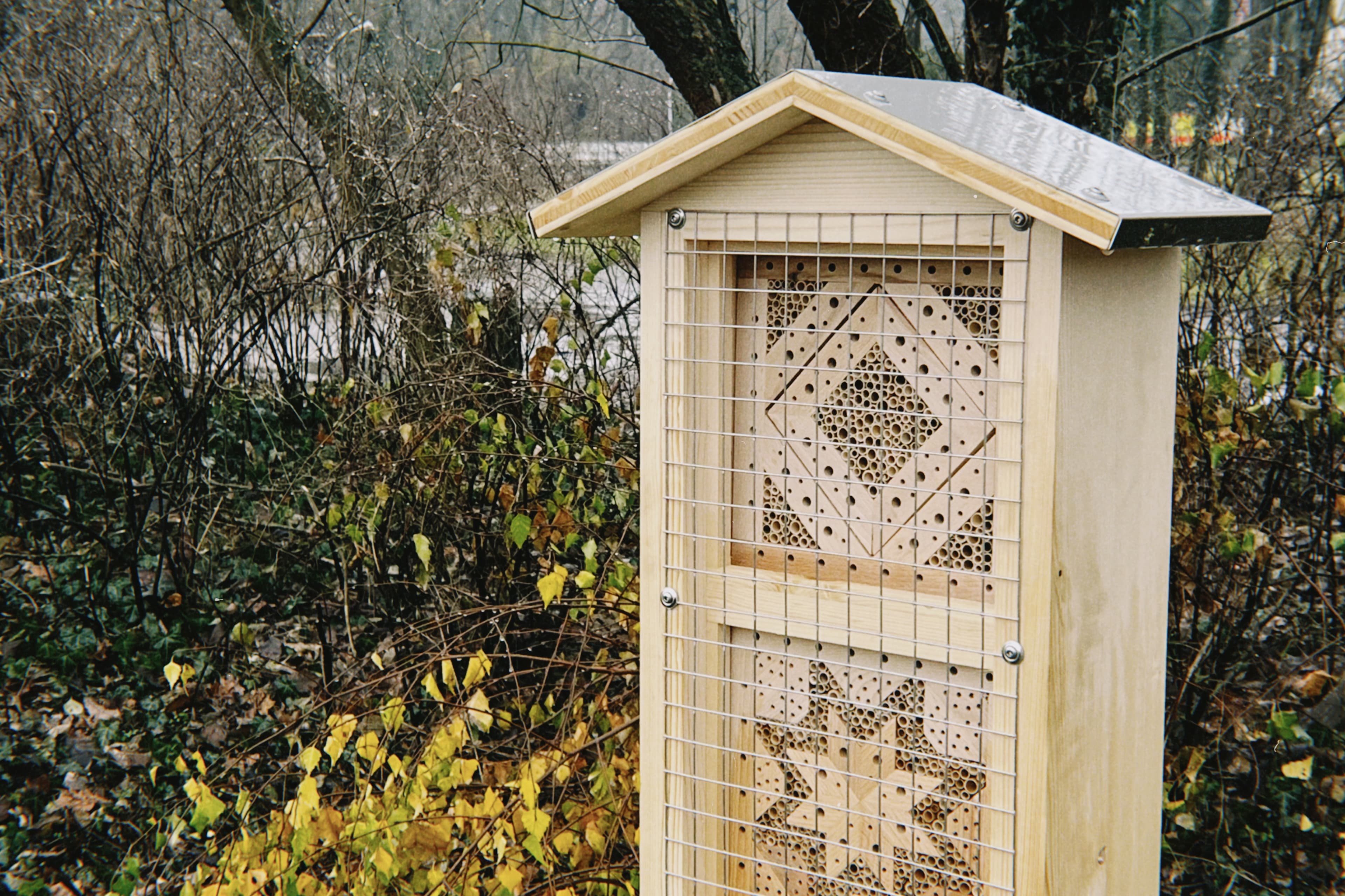Ein Bienenhotel aus Holz steht vor einer Wiese.