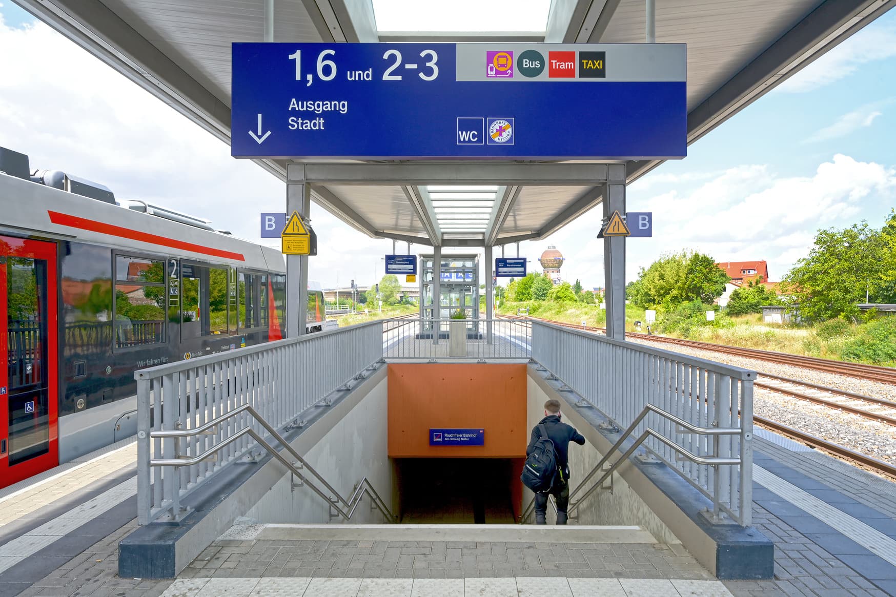 Ein Treppenaufgang am Bahnsteig, darüber ein großes, blaues Schild mit Weg- und Richtungsanweisung.