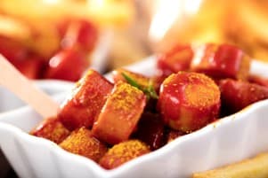 Nahaufnahme einer kleingeschnittenen Wurst mit Ketchup-Sauce und Curry-Pulver.