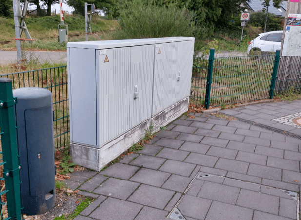 Blick Verteilerkästen. Dahinter ein grüner Zaun.