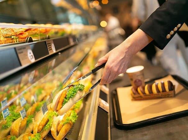 Eine Frau nimmt mit einer Zange ein belegtes Brötchen aus der Auslage.