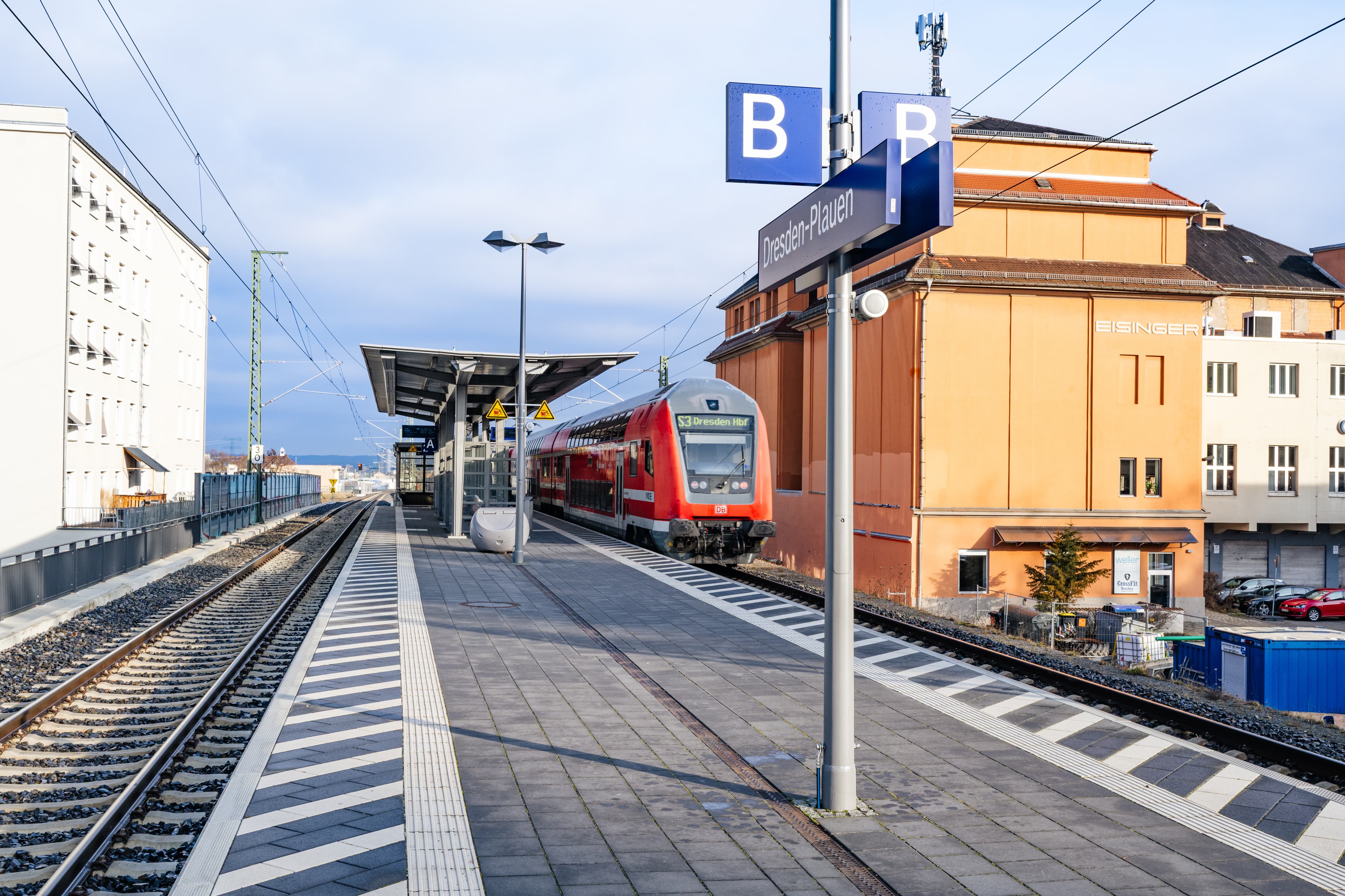 Blick auf den gesamten Bahnsteig mit einem Doppeldeckerzug an einer Bahnsteigkante. Außerdem sieht man das Bahnhofsnamensschild und das Gleisabschnittskennzeichen B 