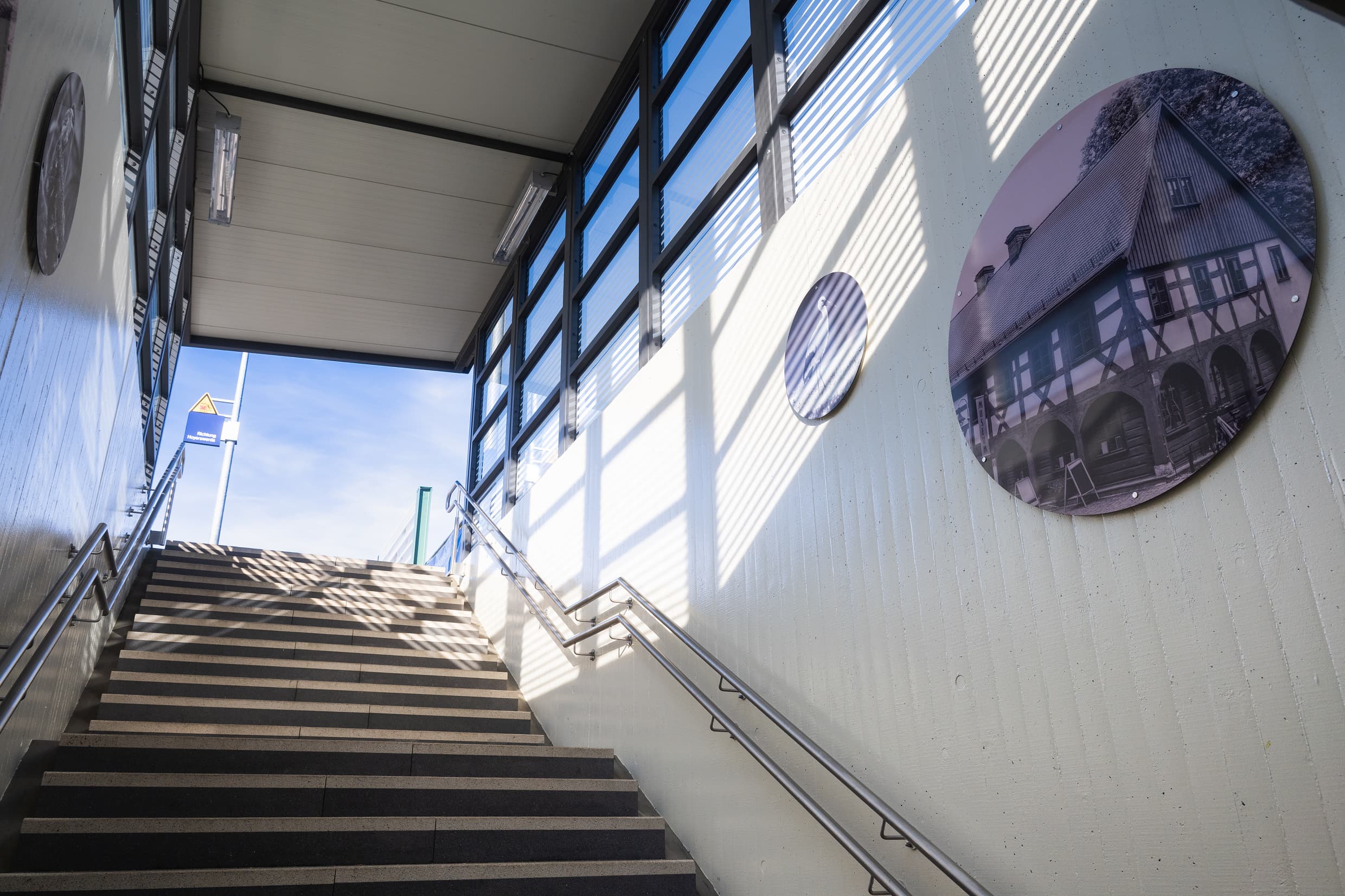 Hellbeige gestrichener Treppenaufgang mit drei verschieden großen Boards mit regionalen Motiven wie dem Storch oder ein Fachwerkhaus.