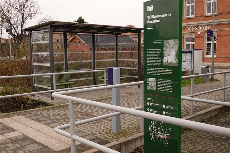 Zu sehen ist im Vordergrund eine Info-Stehle gleich neben dem Weg zu Bahnsteig 1.