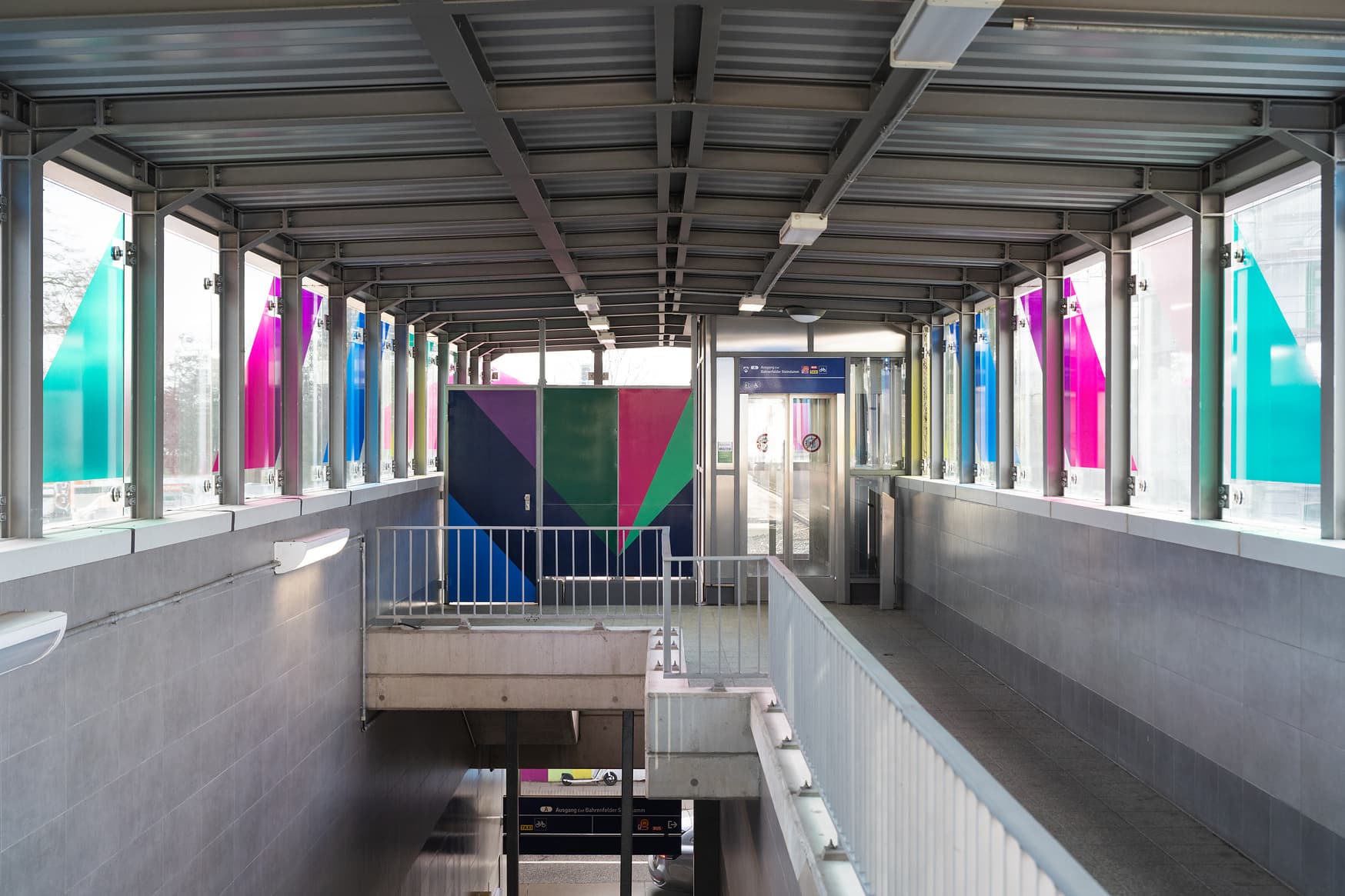 Der Zugangsbereich zum Aufzug, Wände, Geländer und Türen neben dem Aufzug sind bunt gestaltet.