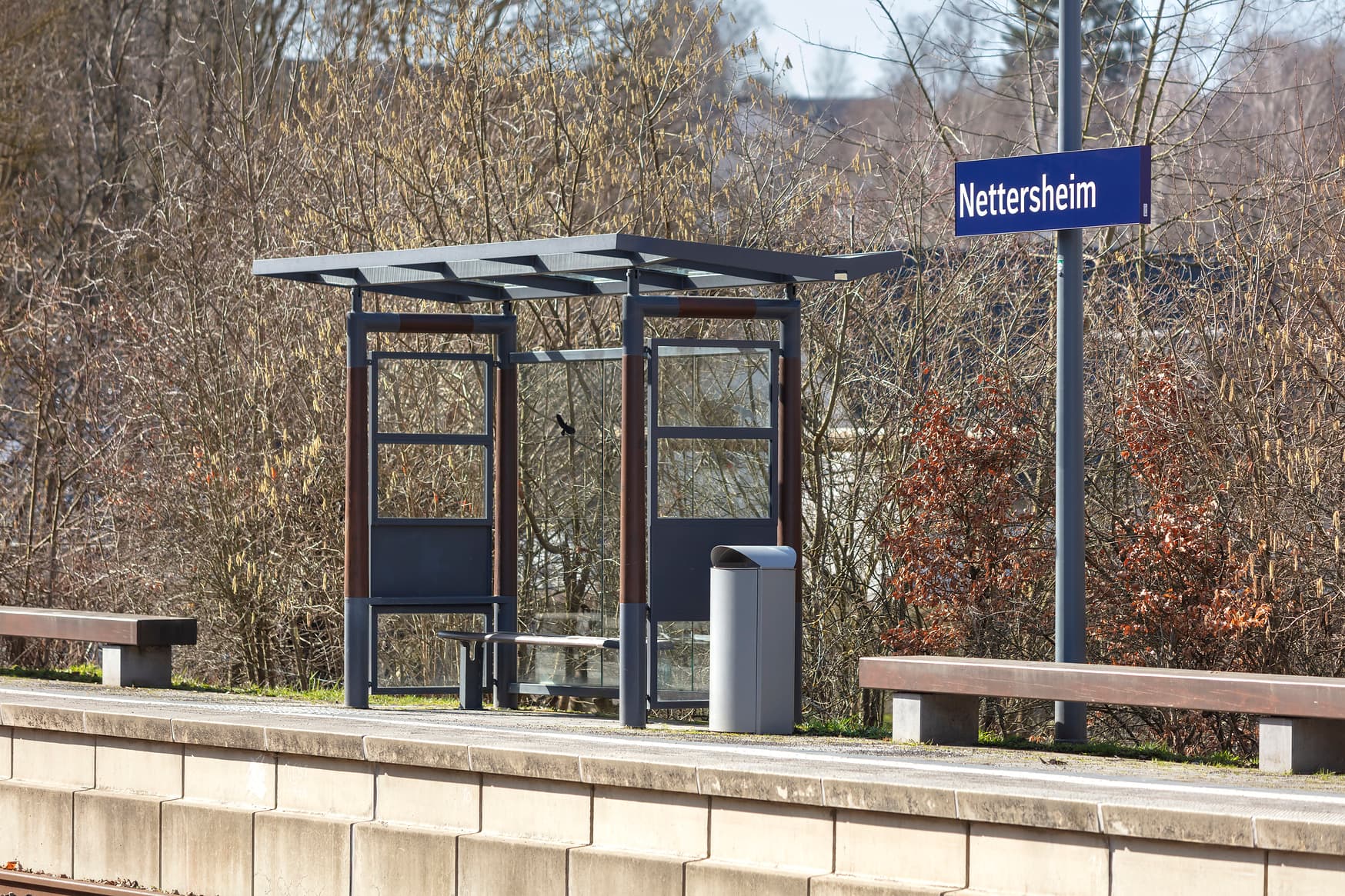 Blick auf ein Wetterschutzhäuschen auf eine Bahnsteig. Rechts und links sind Sitzbänke zu erkennen.