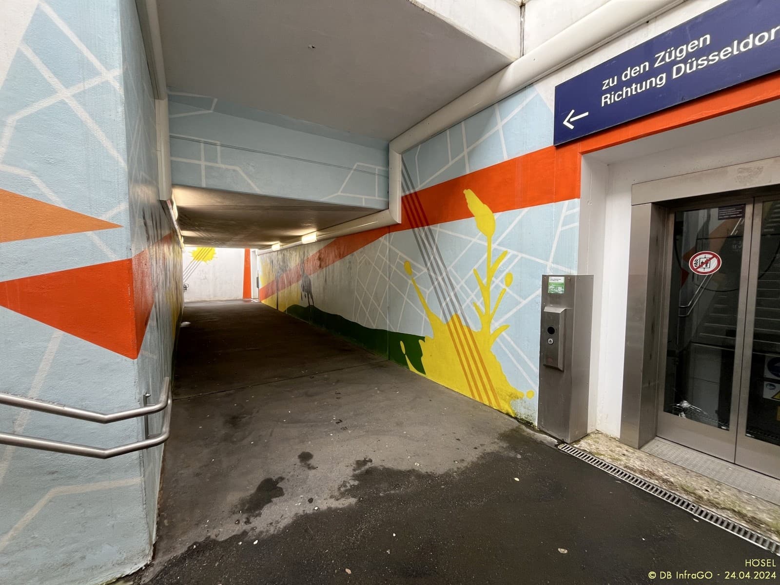 Personenunterführung mit orangen und gelben Grafiken an den Wänden.